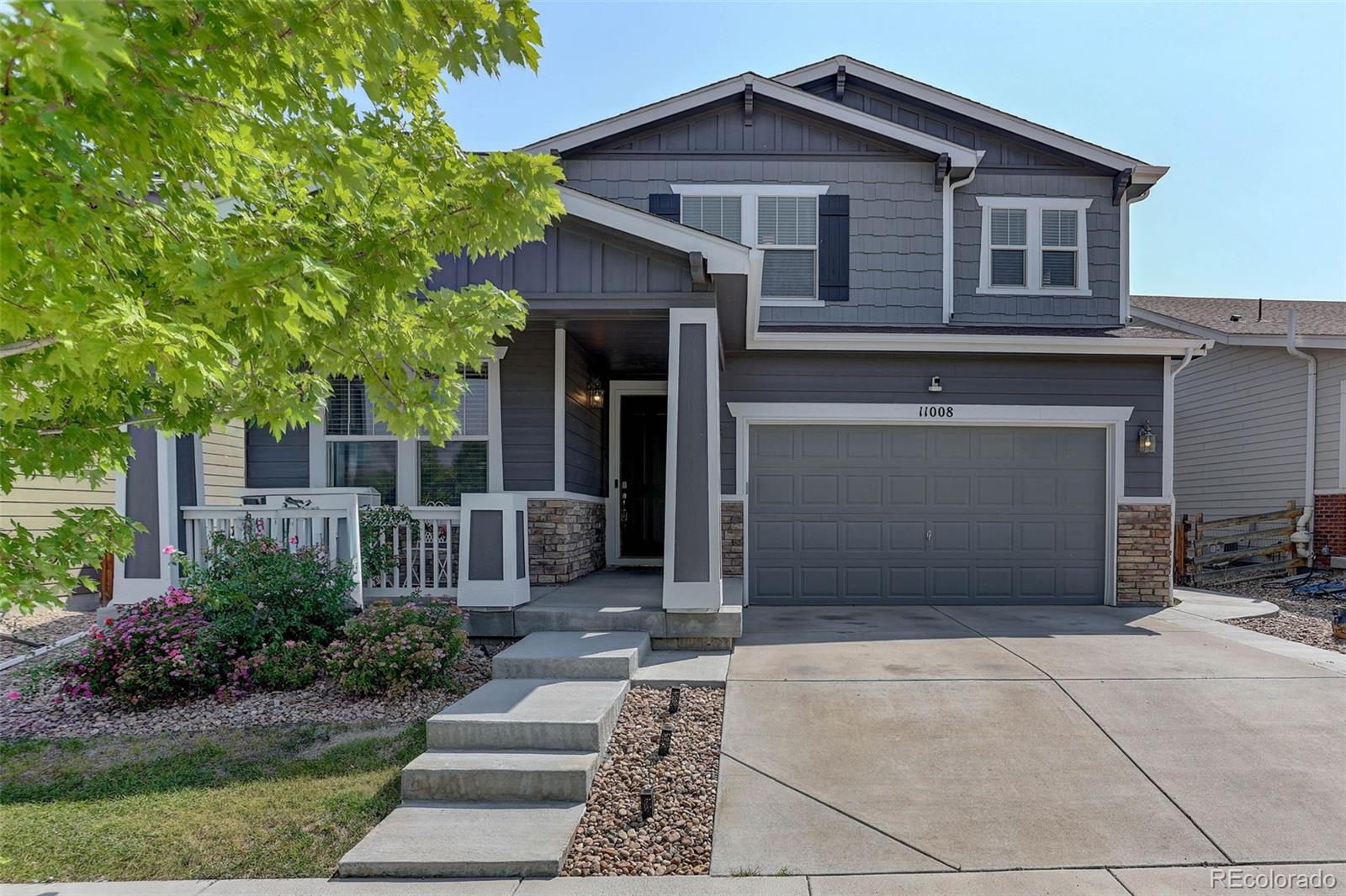 Two-story gray home with a covered porch, attached double garage, and leafy tree in front.