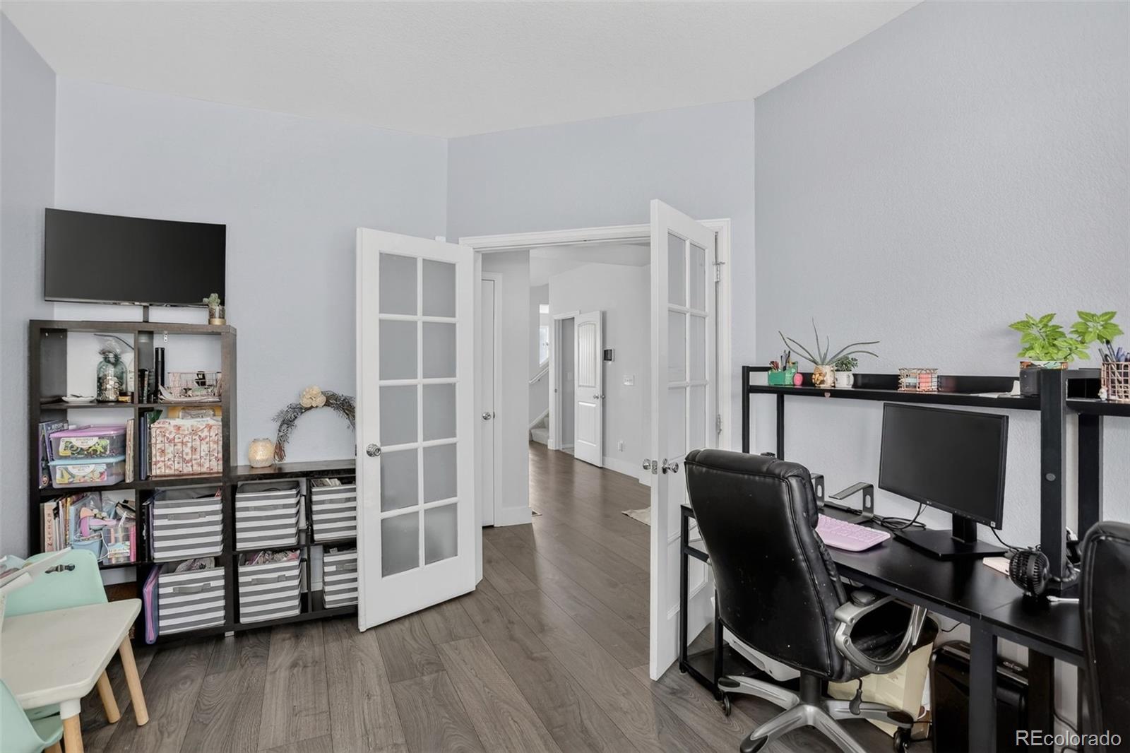 Home office with a black desk and computer, storage shelving, and open French doors.
