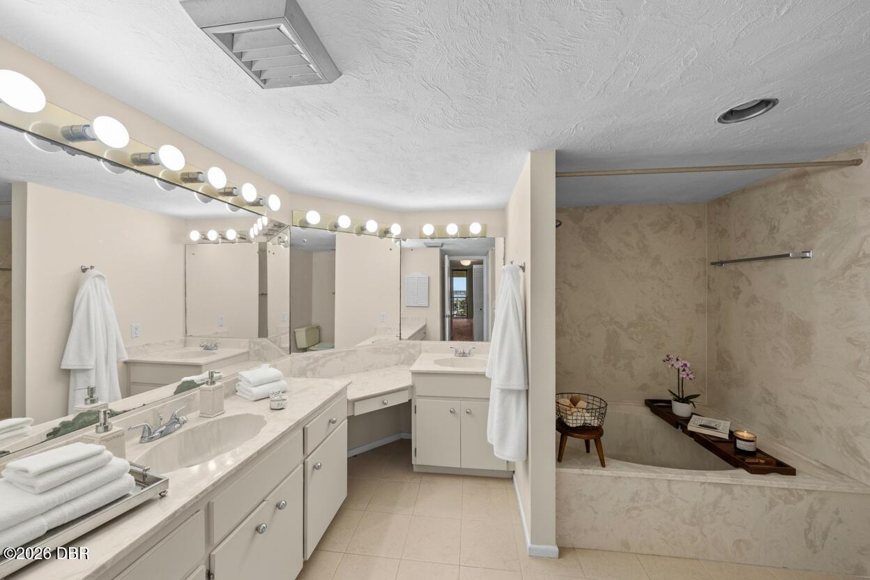 Bathroom with a long double vanity, illuminated mirrors, and a soaking tub with a decorative ledge.