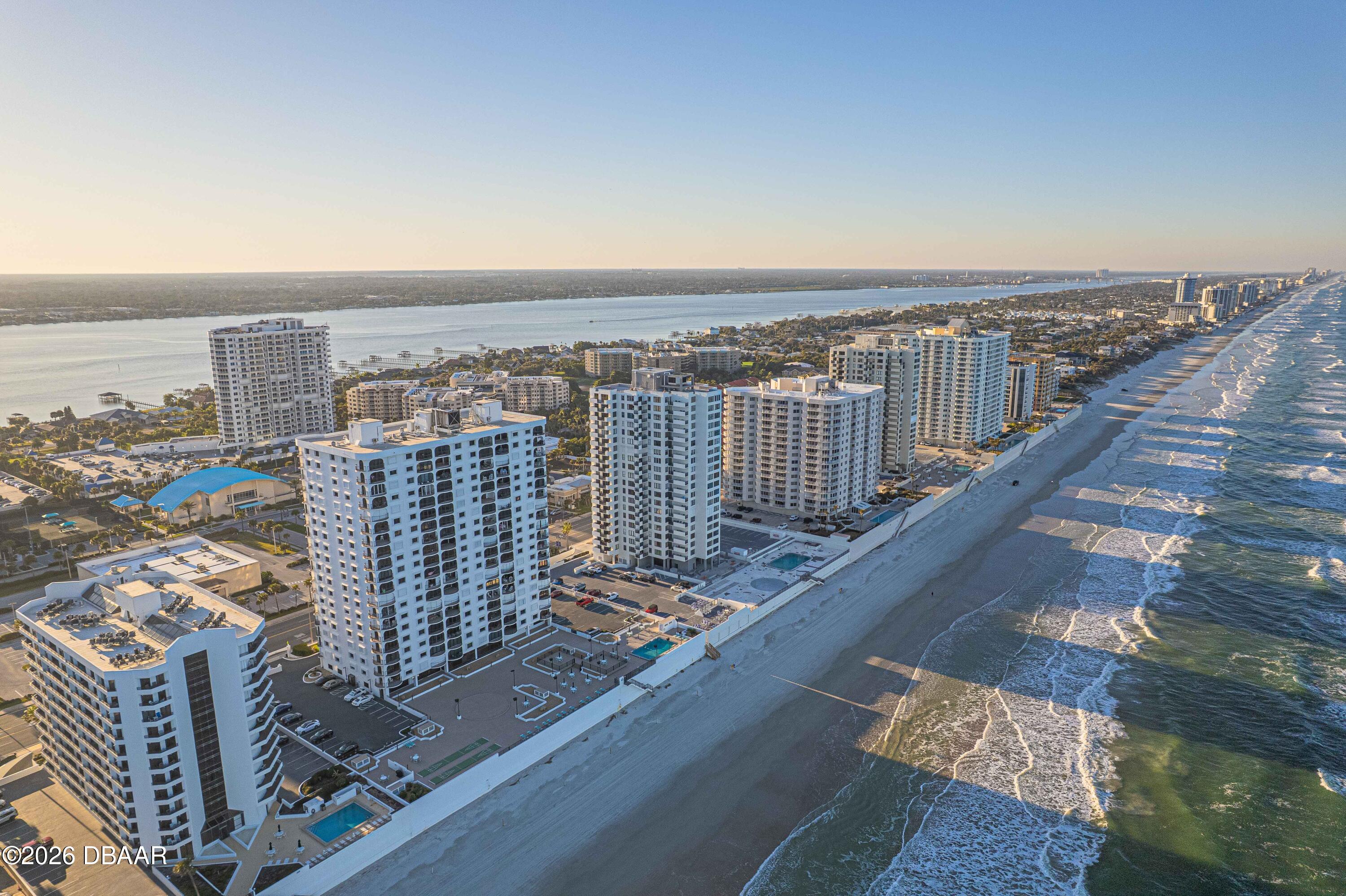 Aerial view of beachfront condominium towers, sandy shoreline, and ocean waves at golden hour.