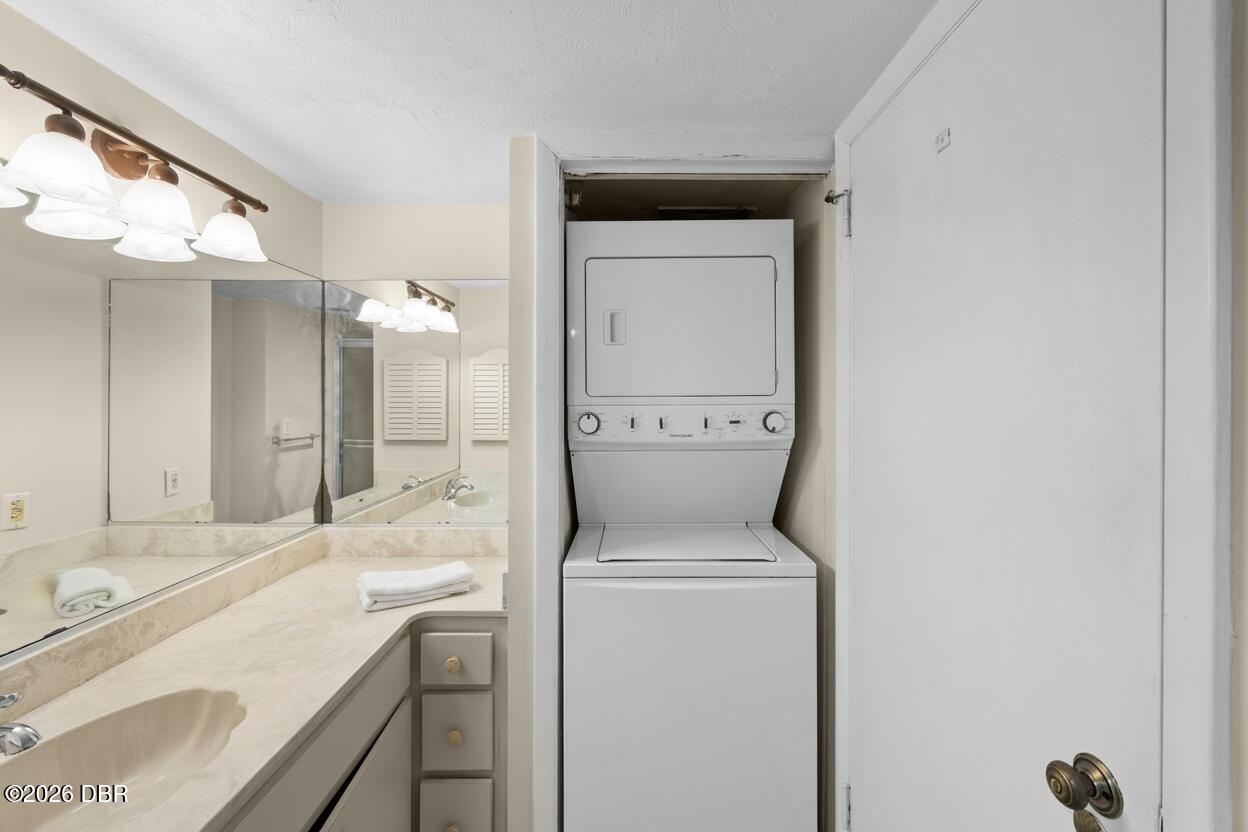 Bathroom vanity with a mirrored counter beside a stacked washer and dryer in a closet.