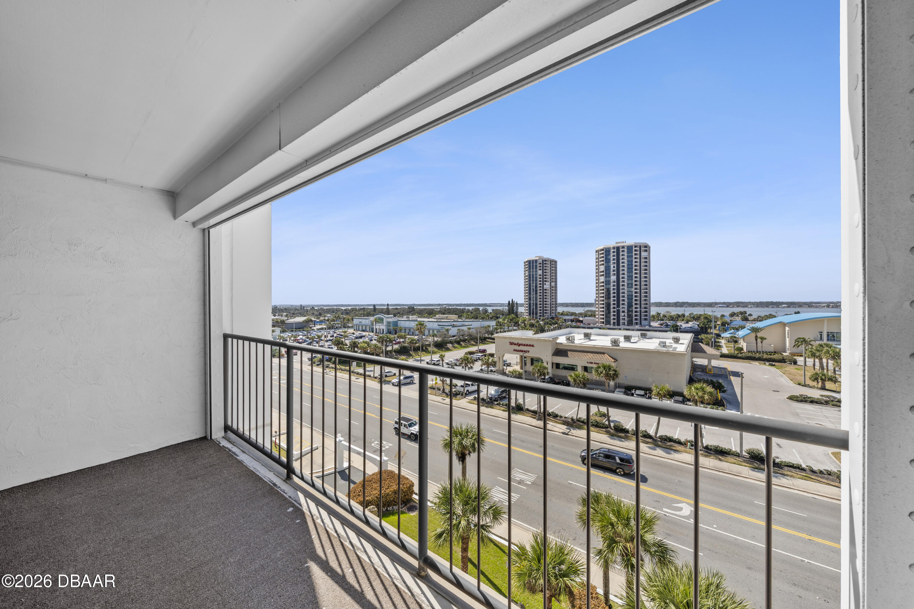 Condominium balcony overlooking a coastal road, two towers, and distant water.