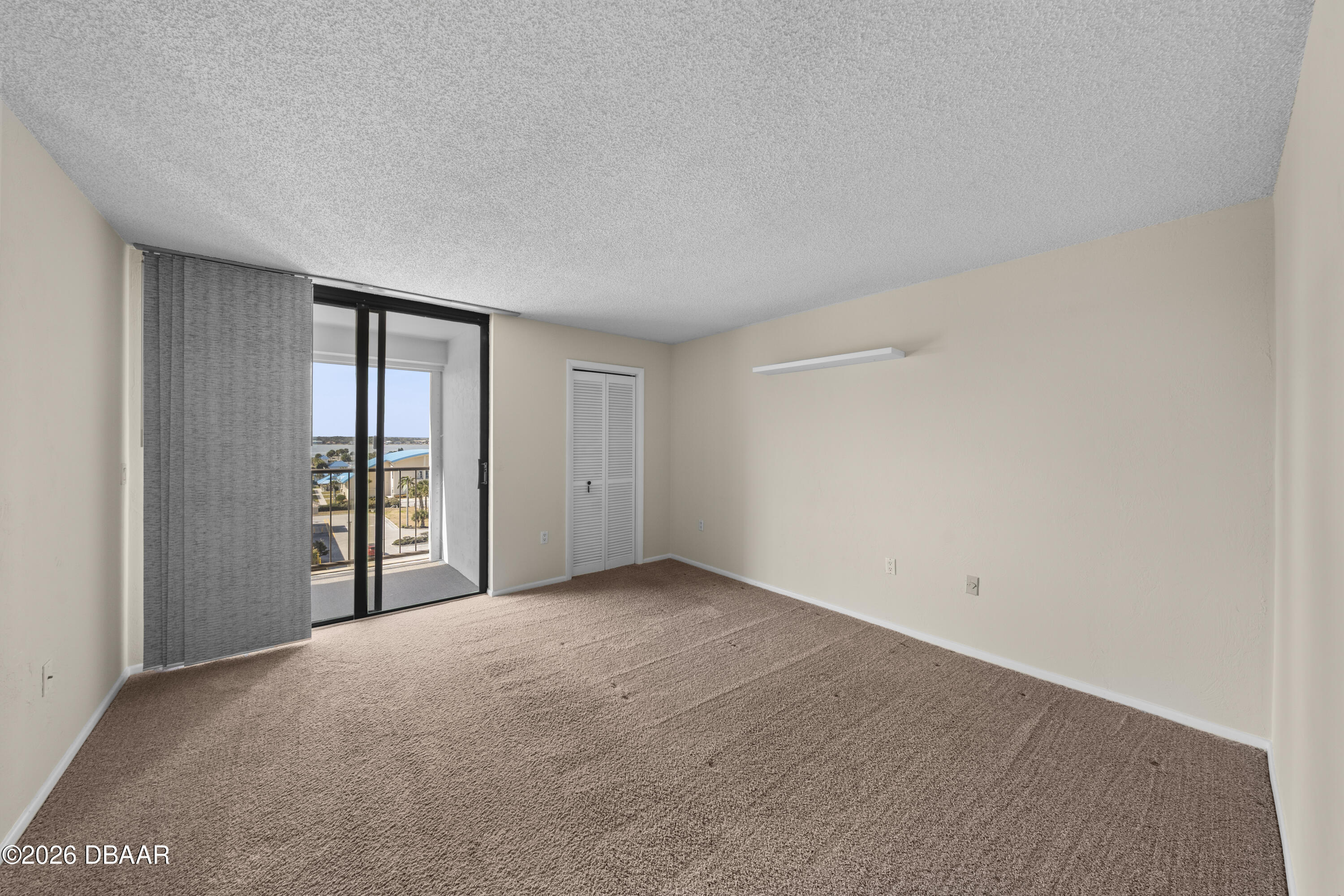 Empty carpeted bedroom with a sliding glass door to a balcony and a louvered closet.