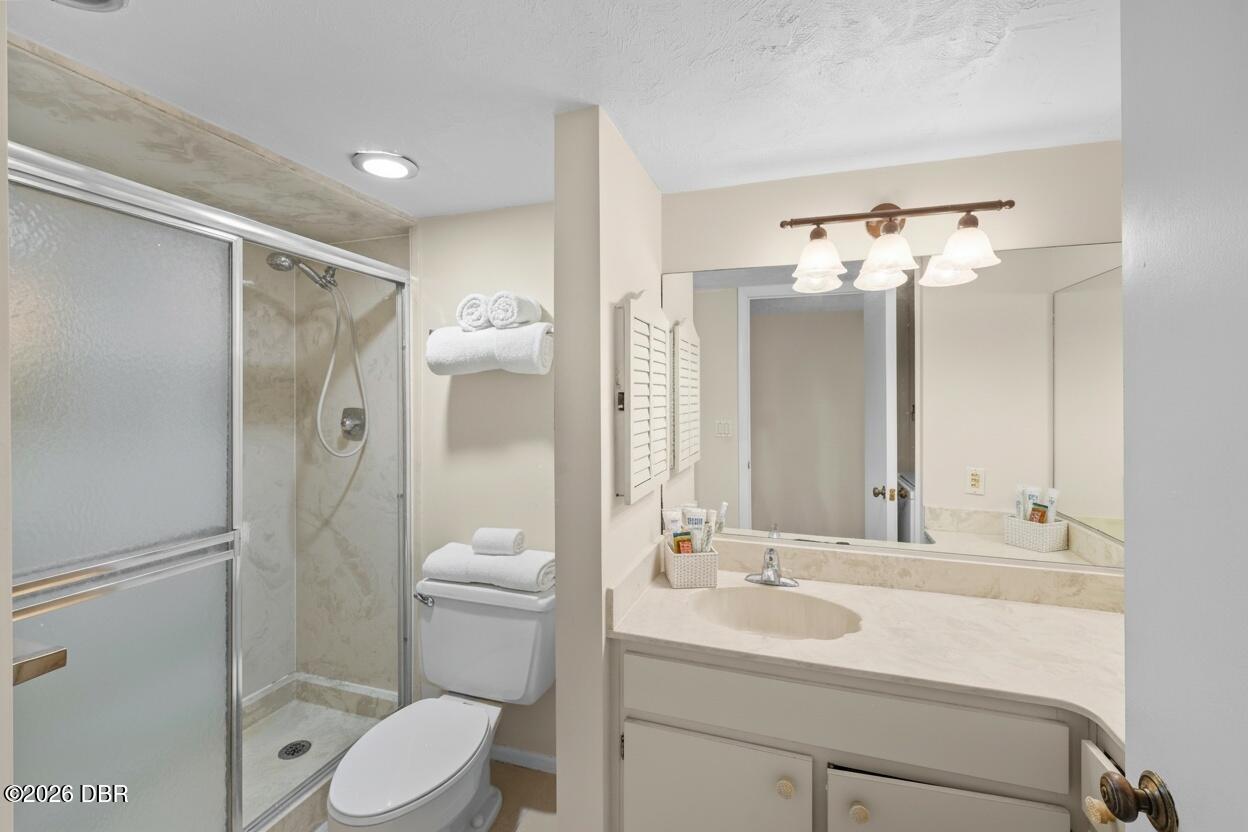 Bathroom with a glass-enclosed shower, toilet, and wide vanity with a large mirror.