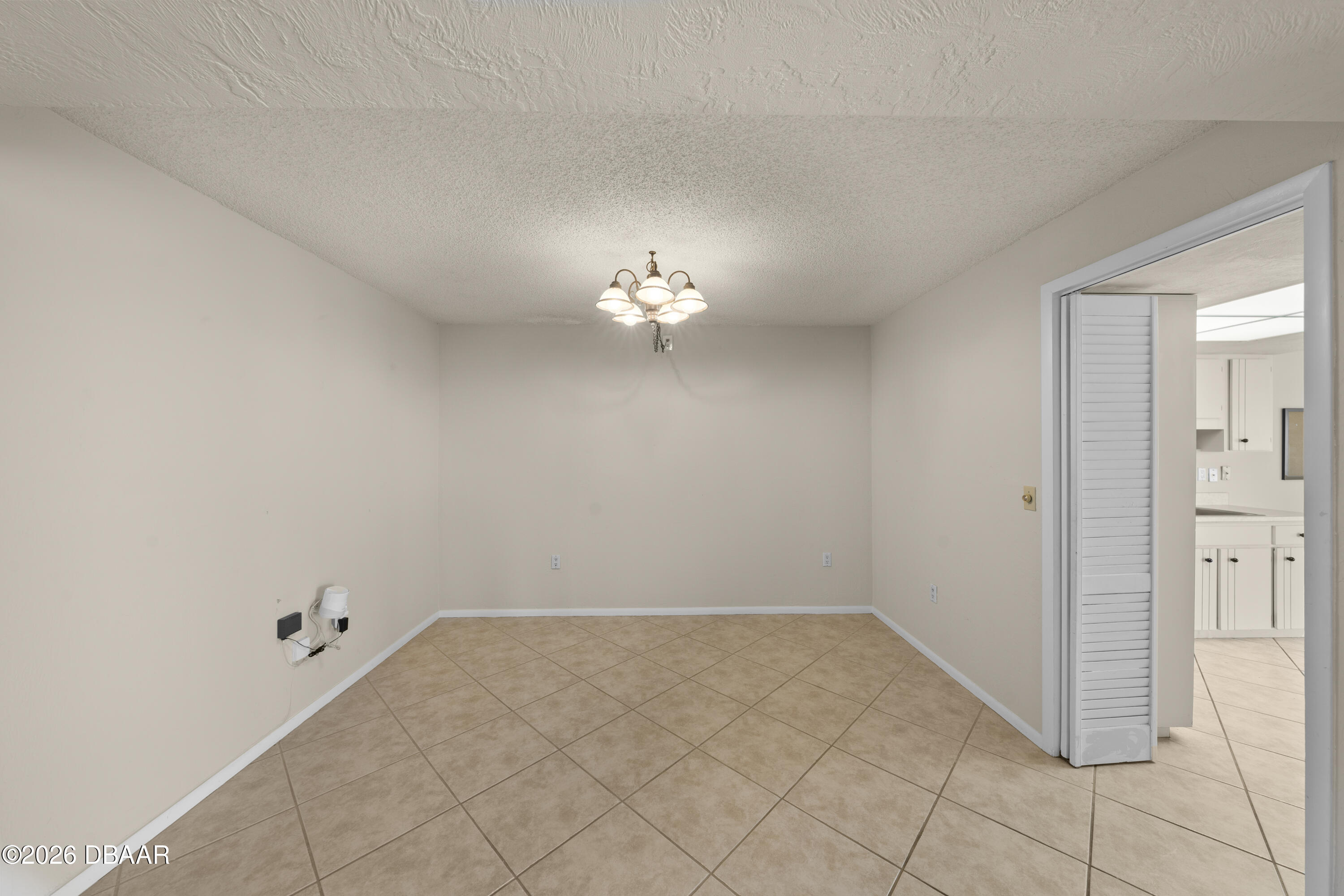 Empty tiled dining room with a chandelier and an open doorway to the kitchen.
