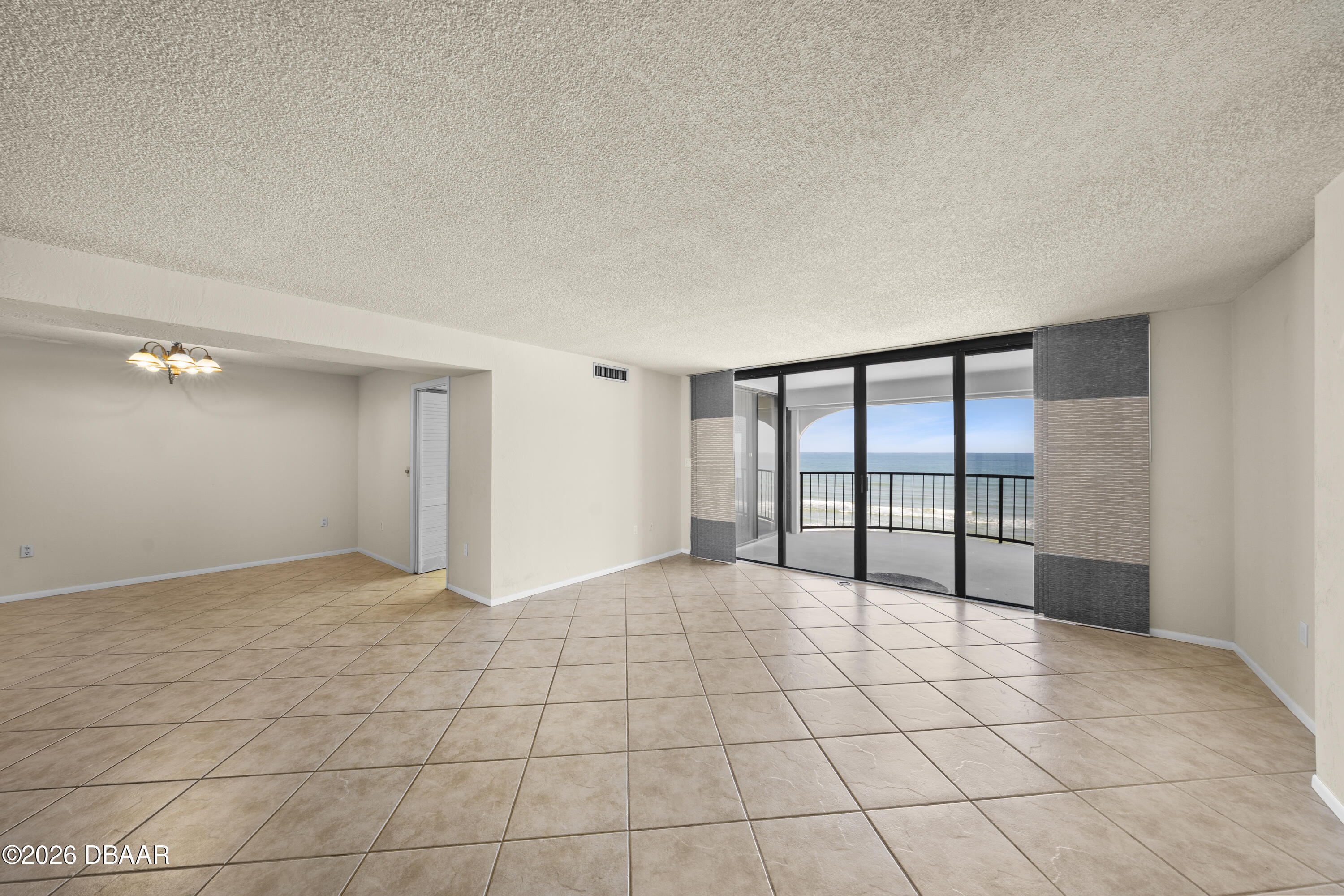 Vacant living room with tiled floors and sliding glass doors opening to an ocean-view balcony.