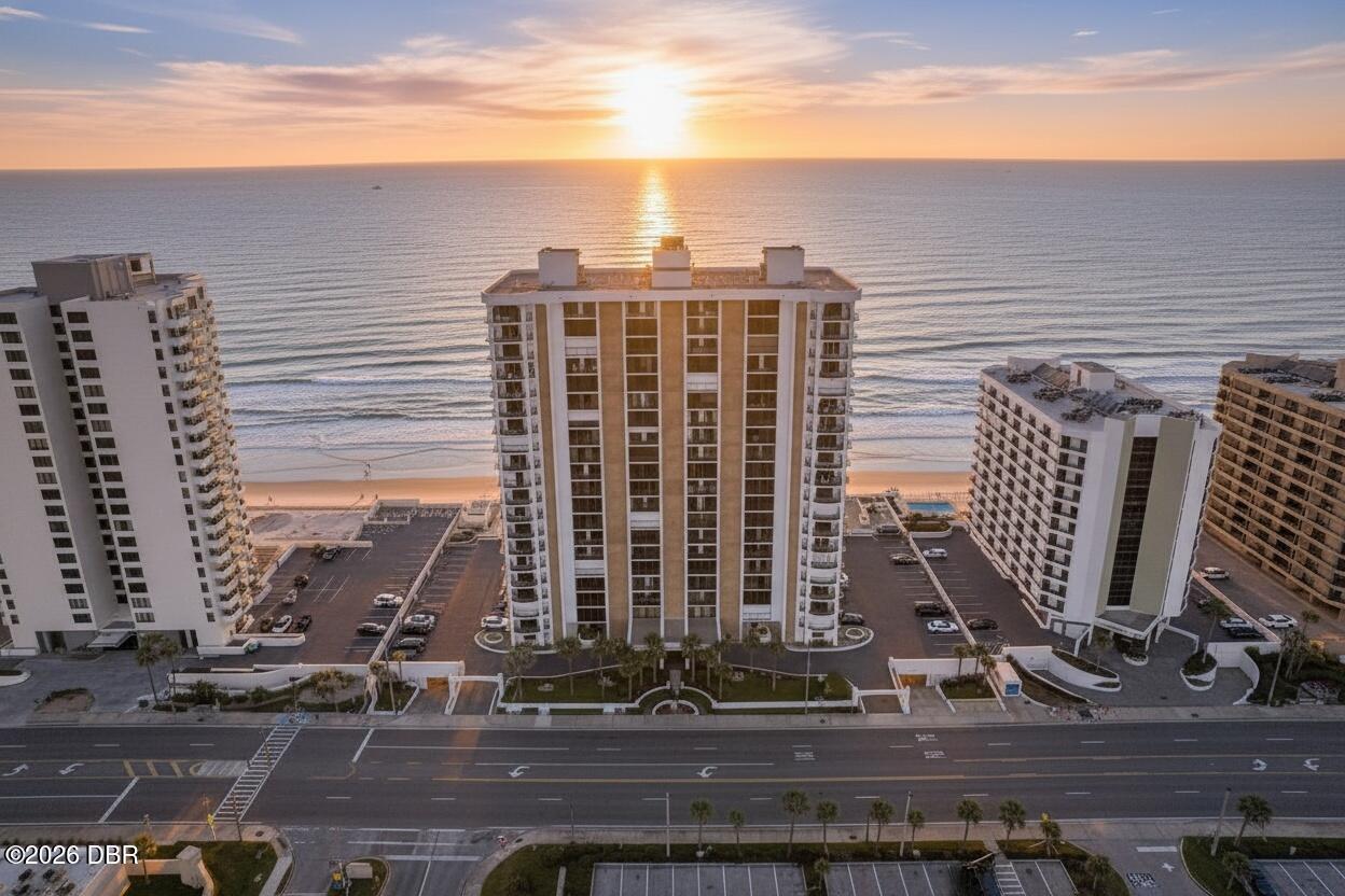 Beachfront condominium towers beside the ocean at sunset, with sunlight reflecting across the water.