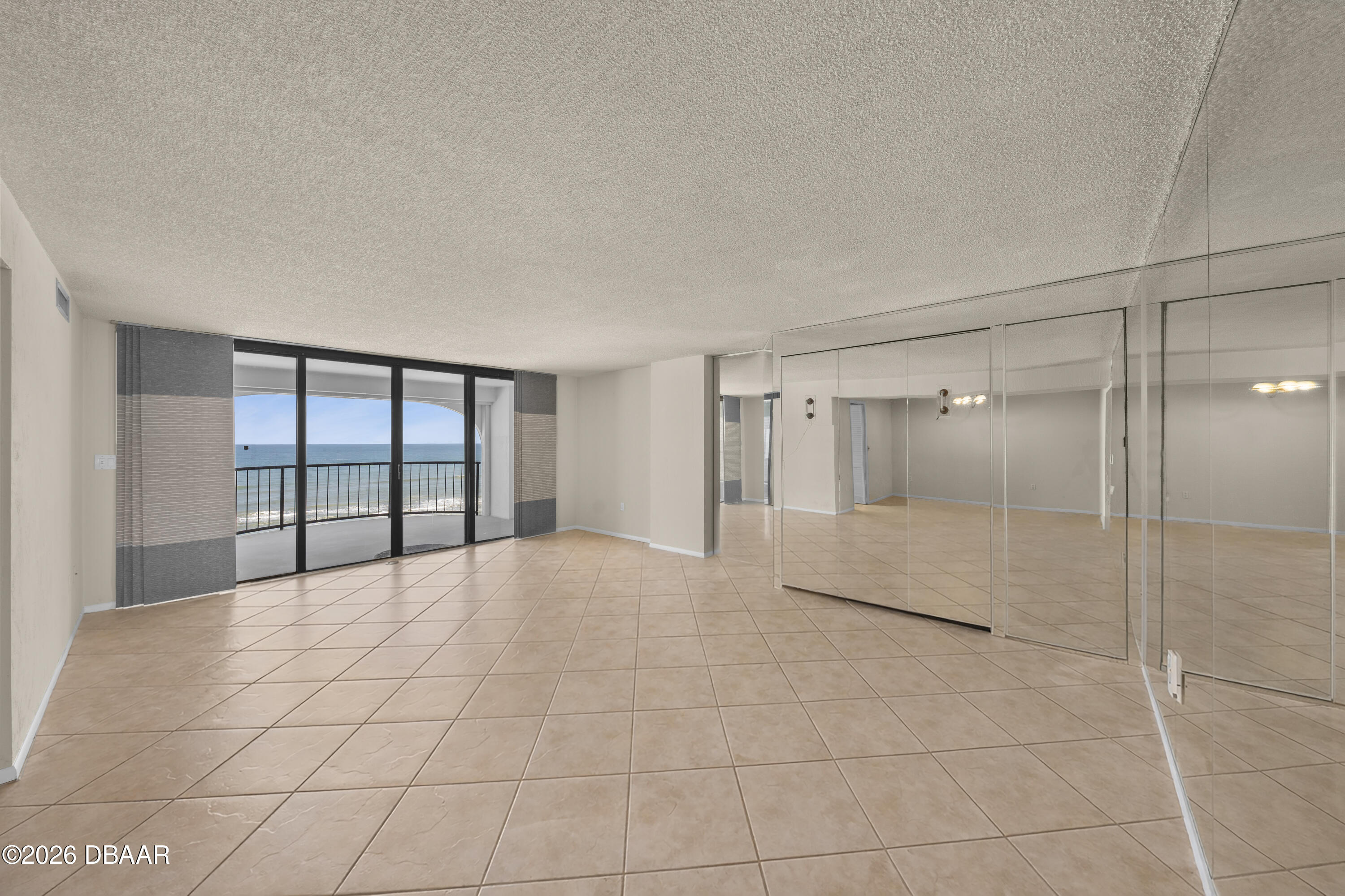 Empty living room with mirrored walls and sliding glass doors opening to an oceanfront balcony.