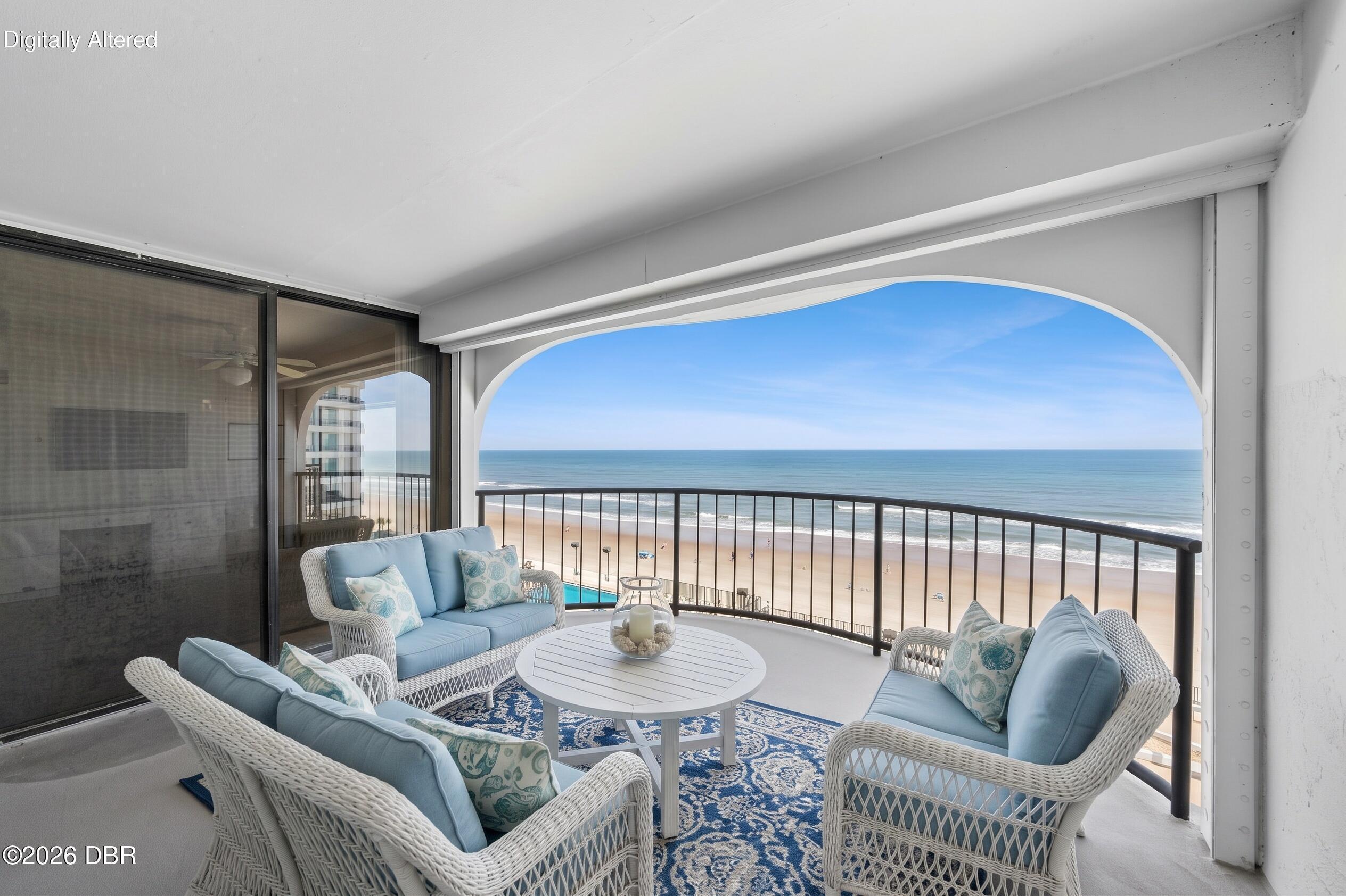 Furnished balcony with wicker seating overlooks the beach and ocean.