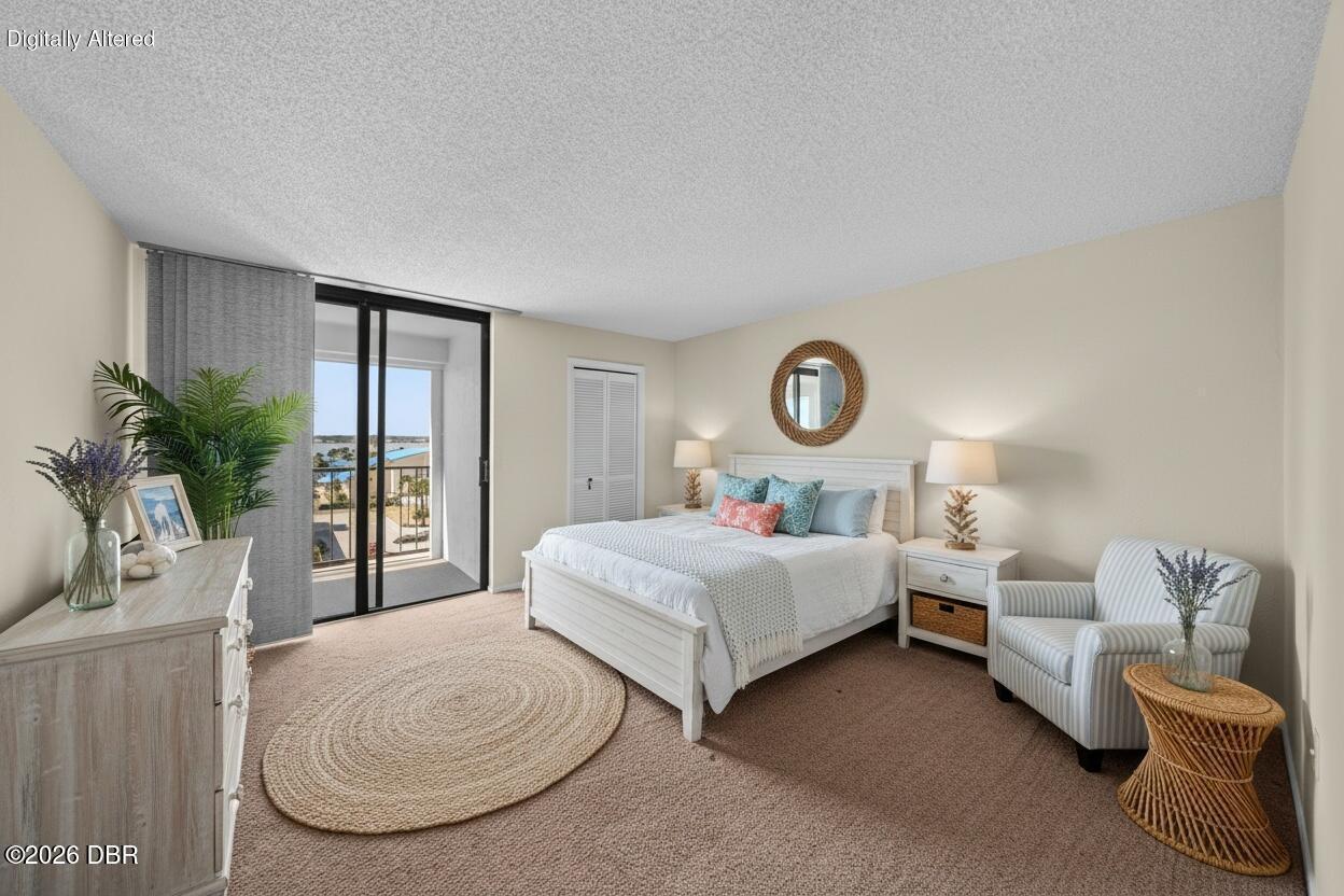 Staged bedroom with a white bed, balcony doors, and a glimpse of water.