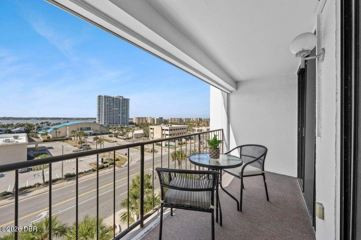 Condo balcony with a small table and chairs overlooking nearby buildings and a strip of water.
