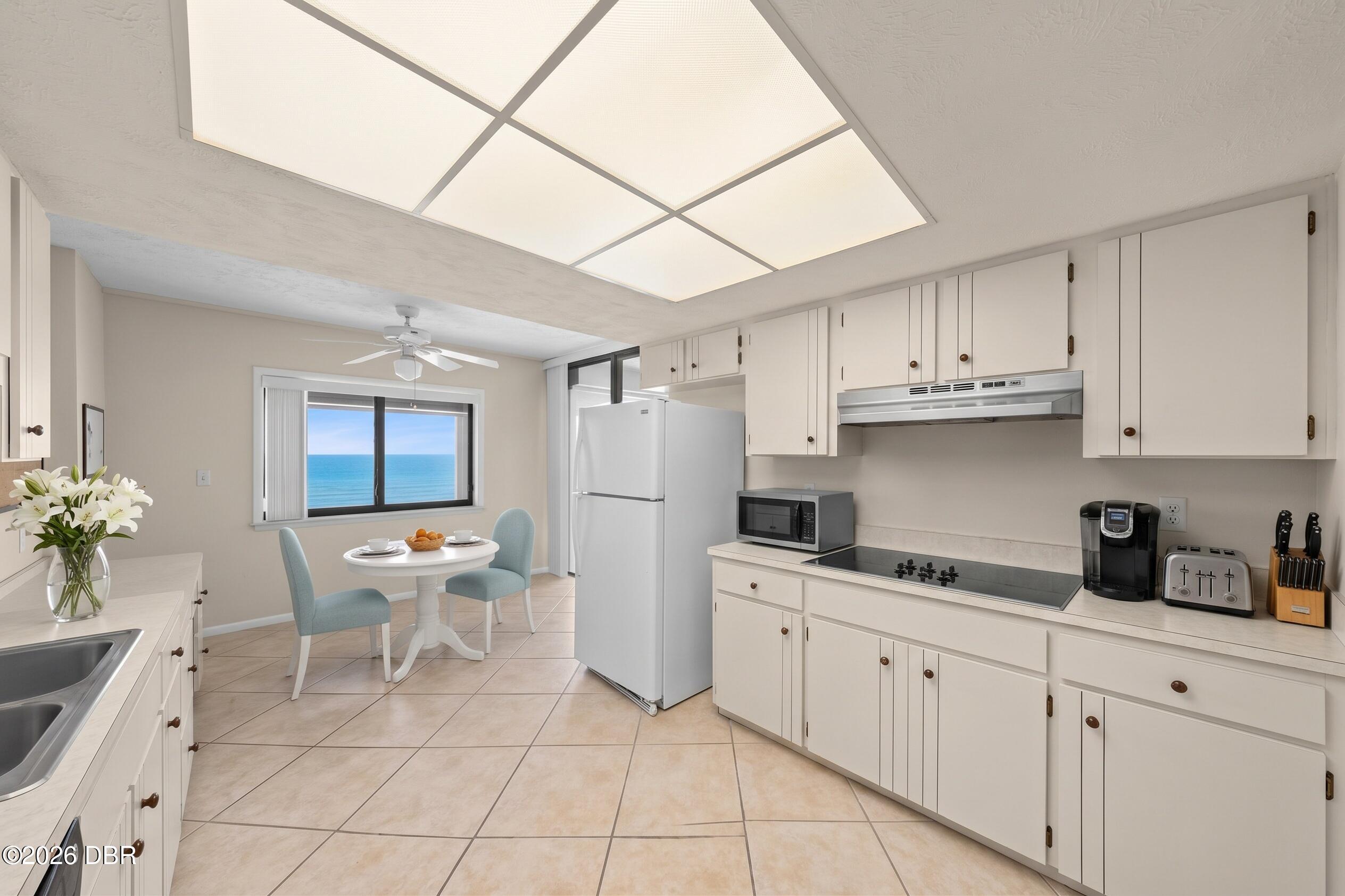 Bright kitchen with white cabinetry, a small dining table, and ocean views through the window.