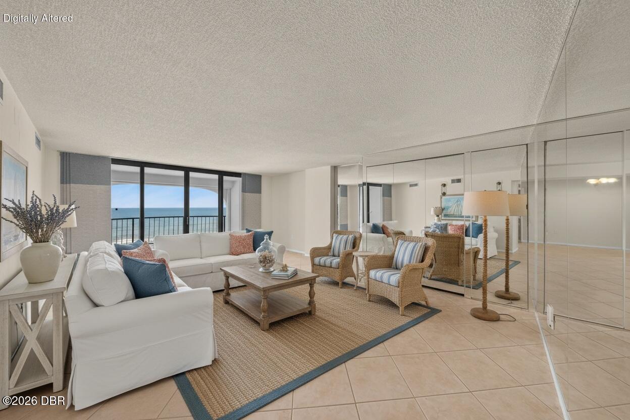 Oceanfront living room with white sectional, wicker chairs, and mirrored walls.