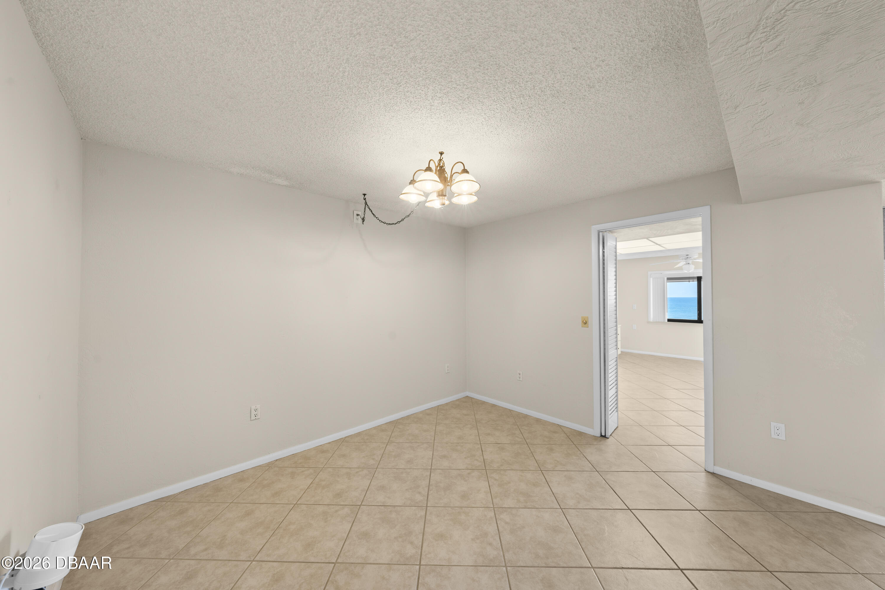 Empty tiled dining area with a chandelier, opening to a room with an ocean view.