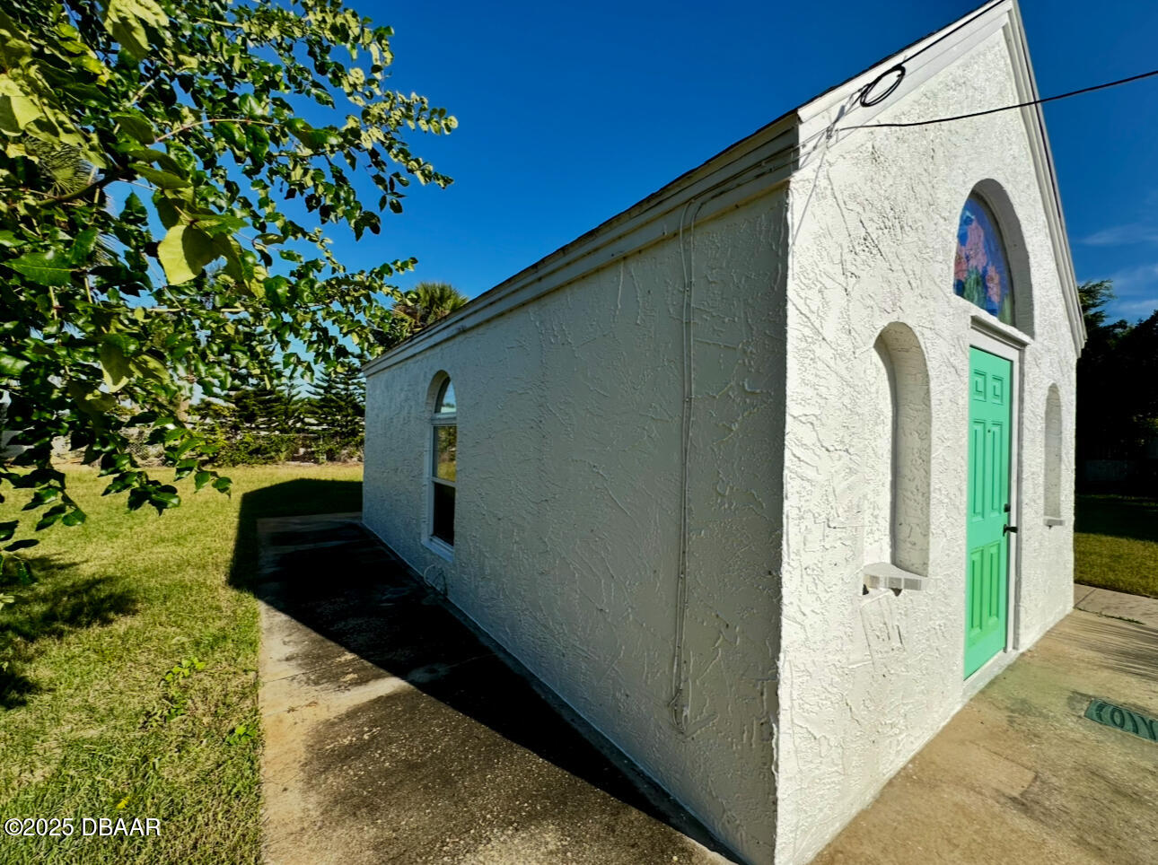 Small white stucco cottage with a bright green door and arched stained-glass window.