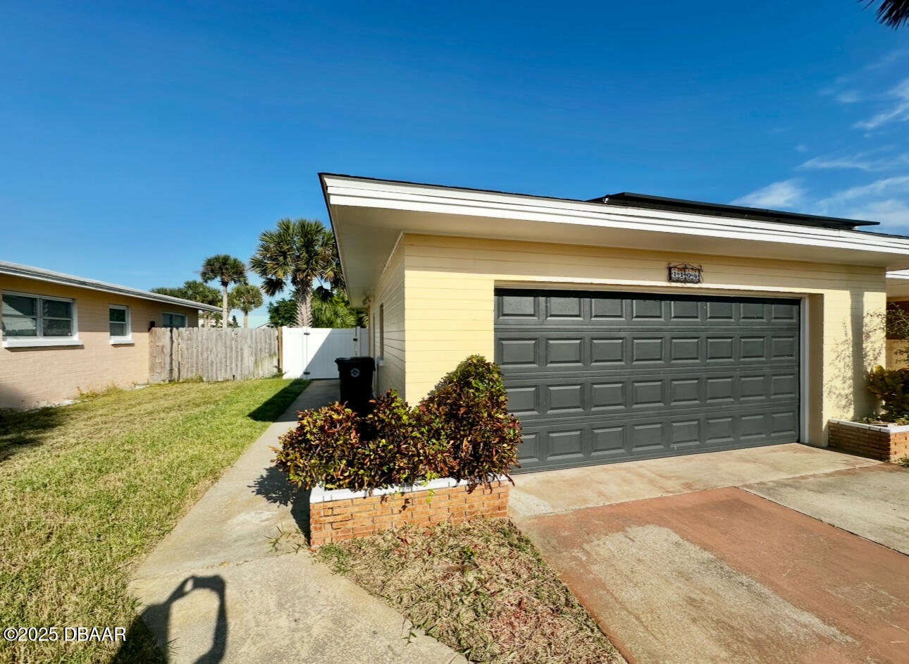 Cottage exterior with pale yellow siding, a wide gray garage door, and brick planters.