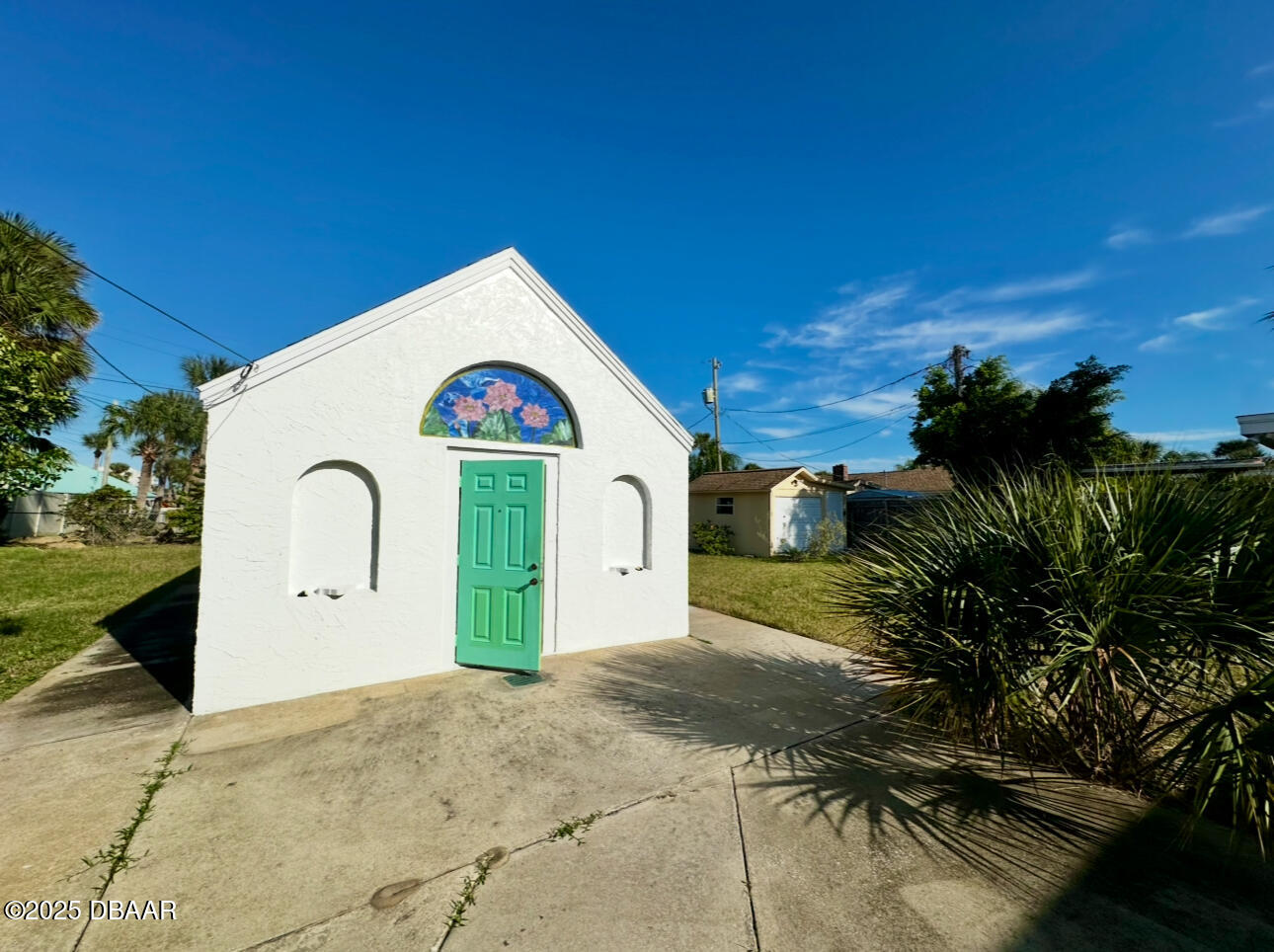White stucco cottage with a green door and colorful floral glass above the entrance.