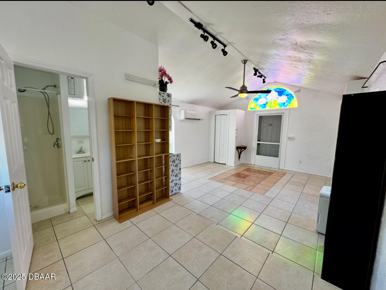 Tiled cottage interior with vaulted ceiling, stained-glass window, and open bathroom doorway.