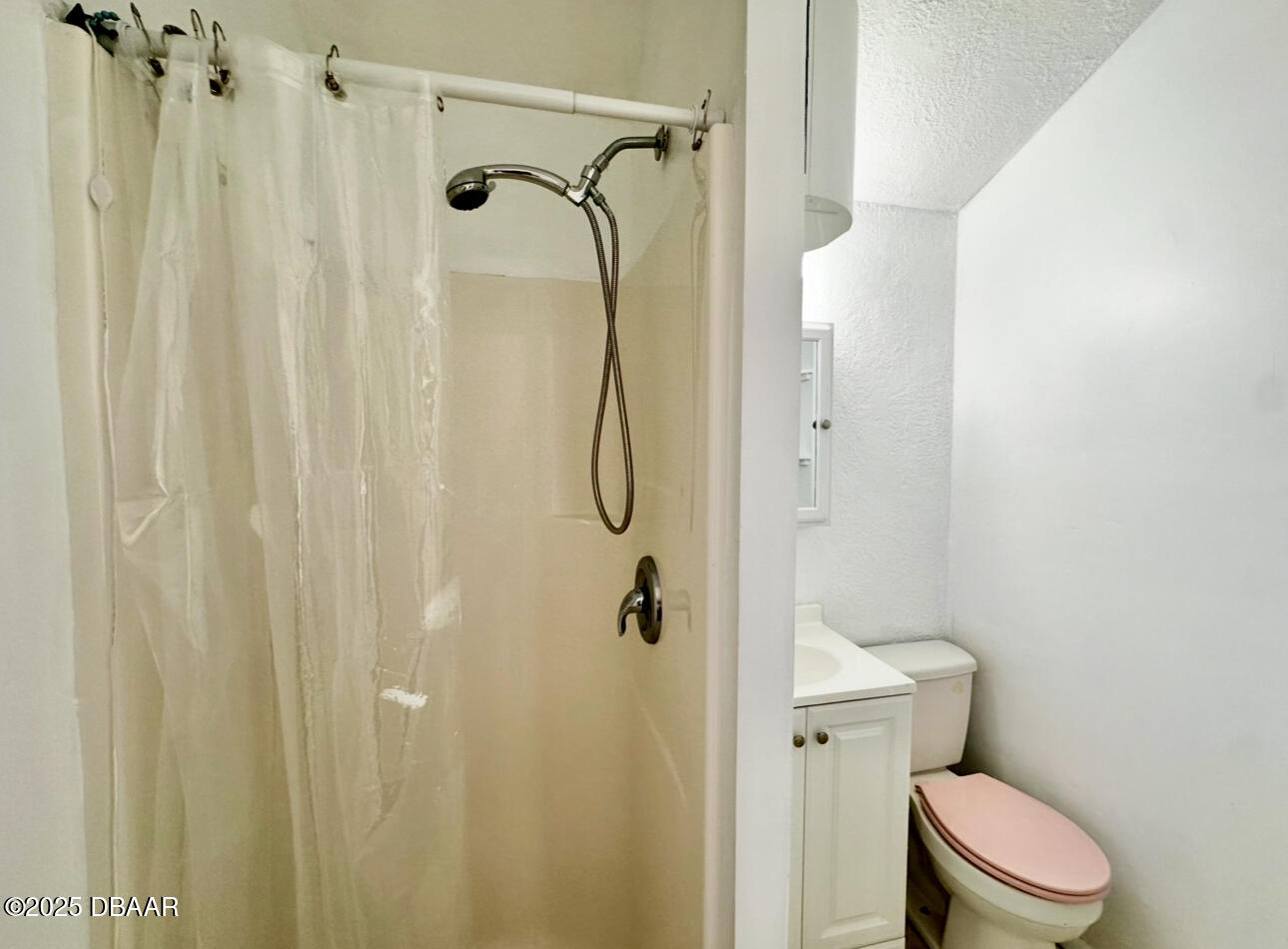 Bathroom with a curtained shower, handheld showerhead, white vanity, and toilet with a pink seat cover.