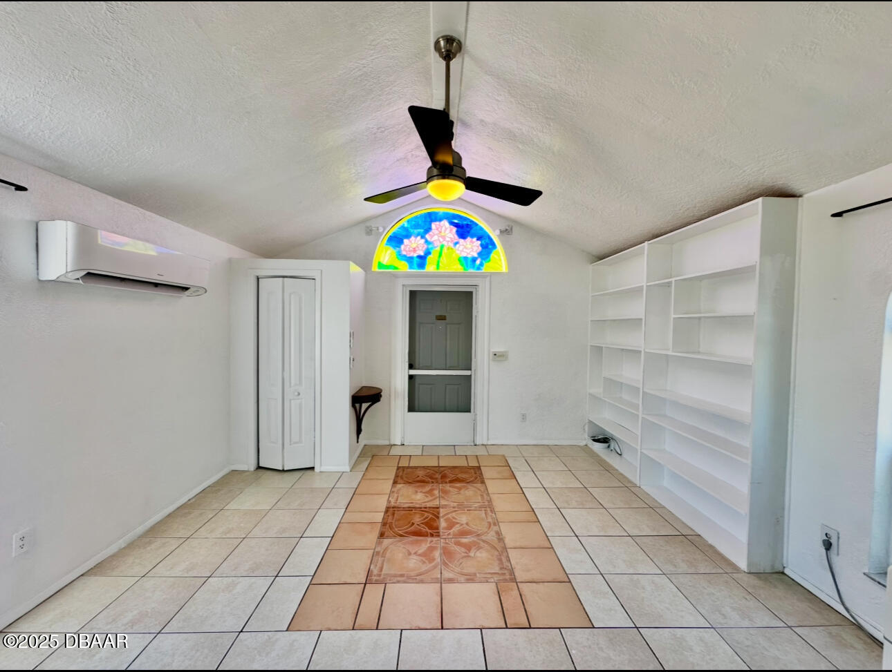 Vacant tiled room with built-in shelves, a black ceiling fan, and a colorful stained-glass window.