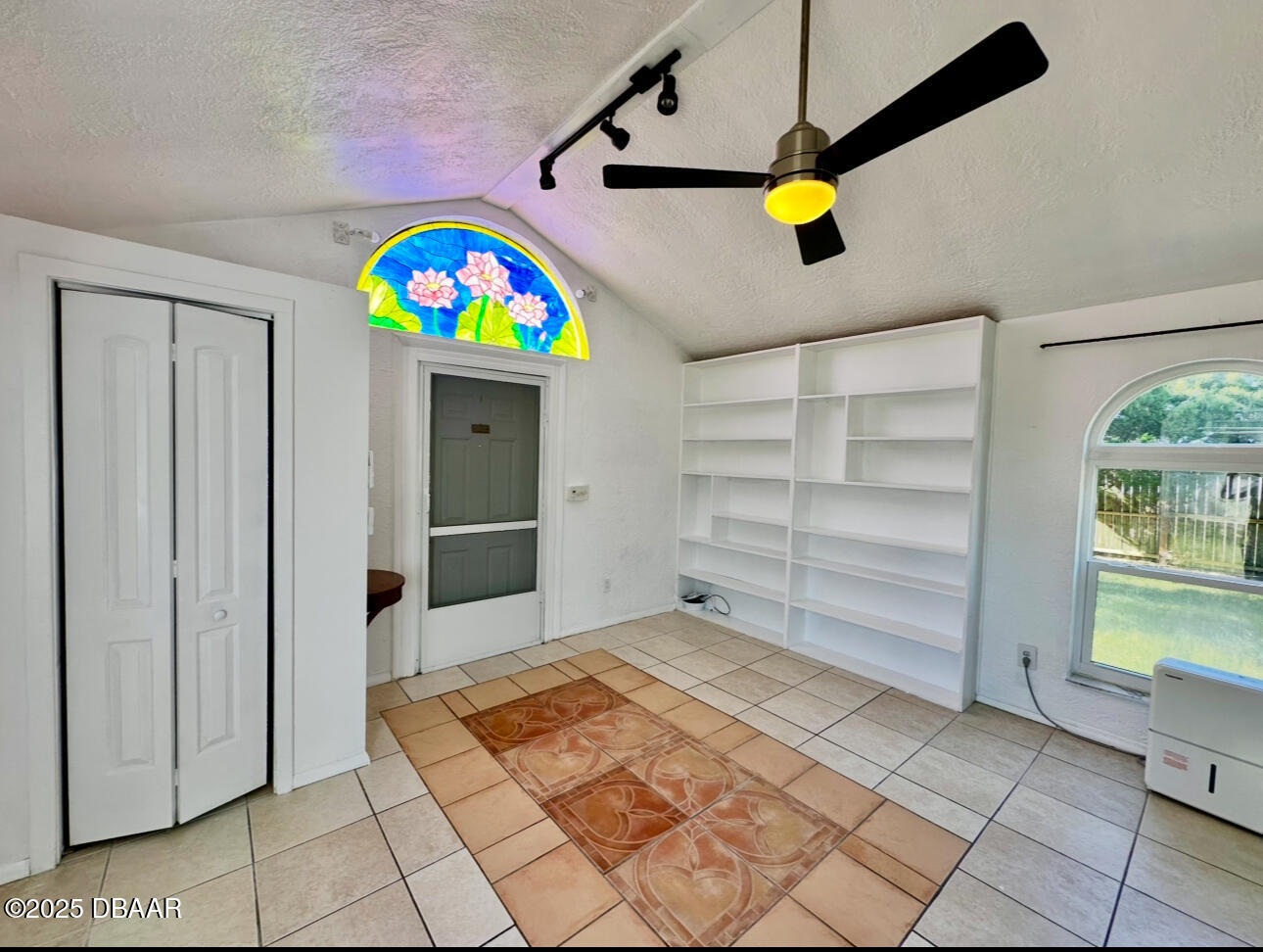 Vacant tiled room with built-in shelving and a colorful stained-glass window above the exterior door.