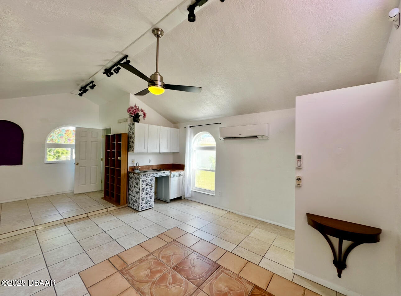 Room with a compact kitchenette, vaulted ceiling, arched windows, and patterned tile floor.
