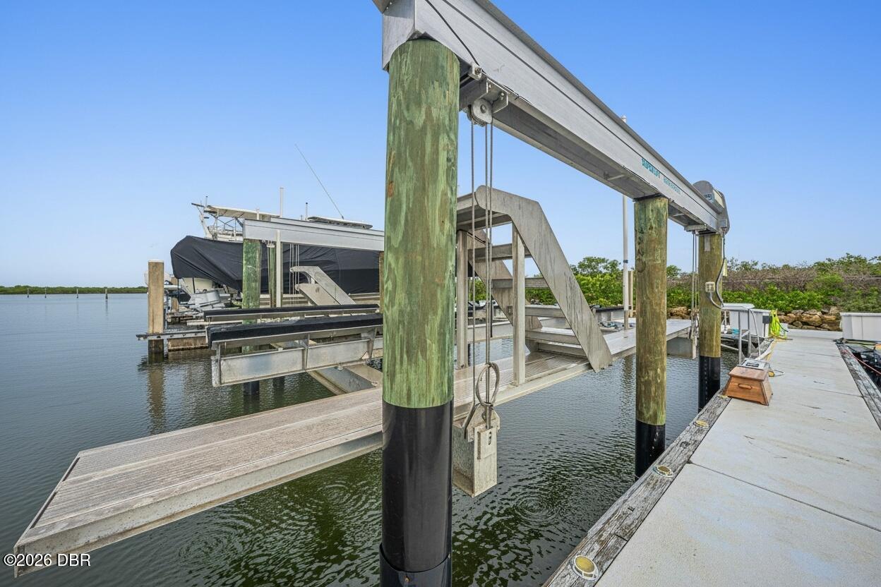 Waterfront boat dock with a metal boat lift and green pilings beside calm water.