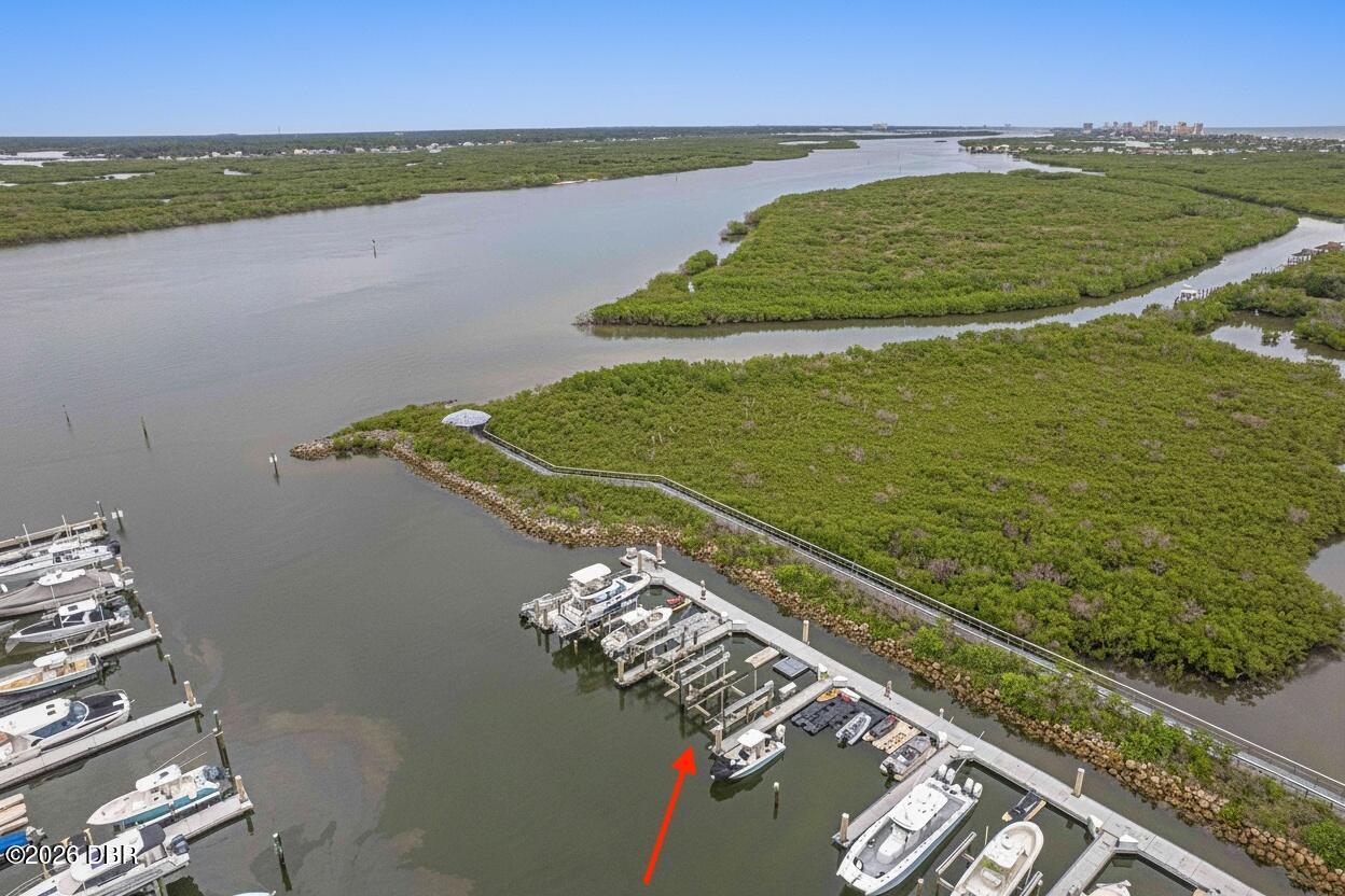 Aerial view of a marina beside a winding river and expansive green marshland.
