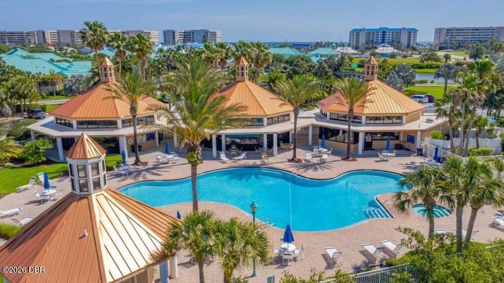 Outdoor pool surrounded by palm trees and pavilion-style buildings, with the ocean in the distance.