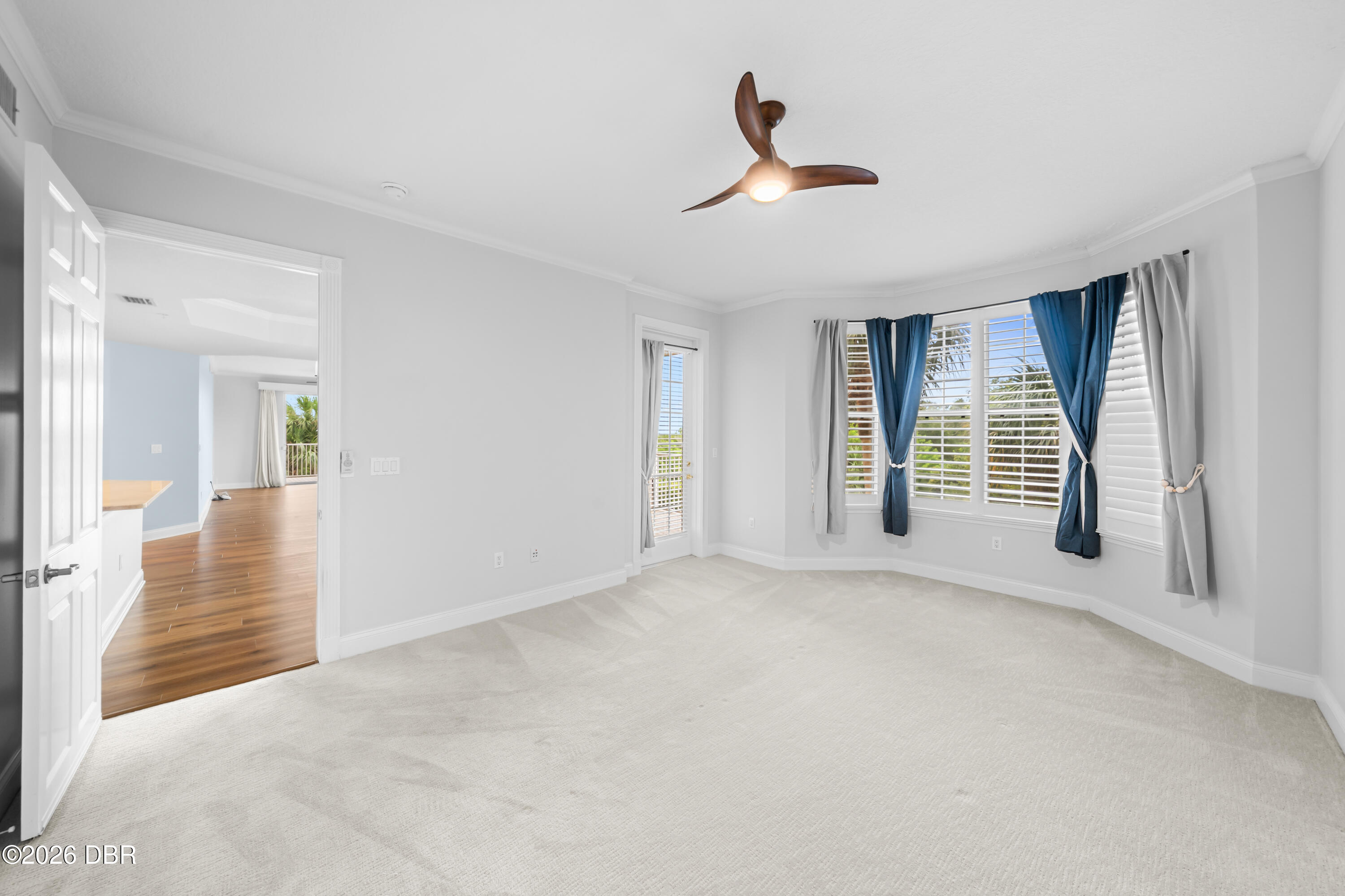 Empty carpeted bedroom with a ceiling fan and wide windows dressed in blue and gray curtains.