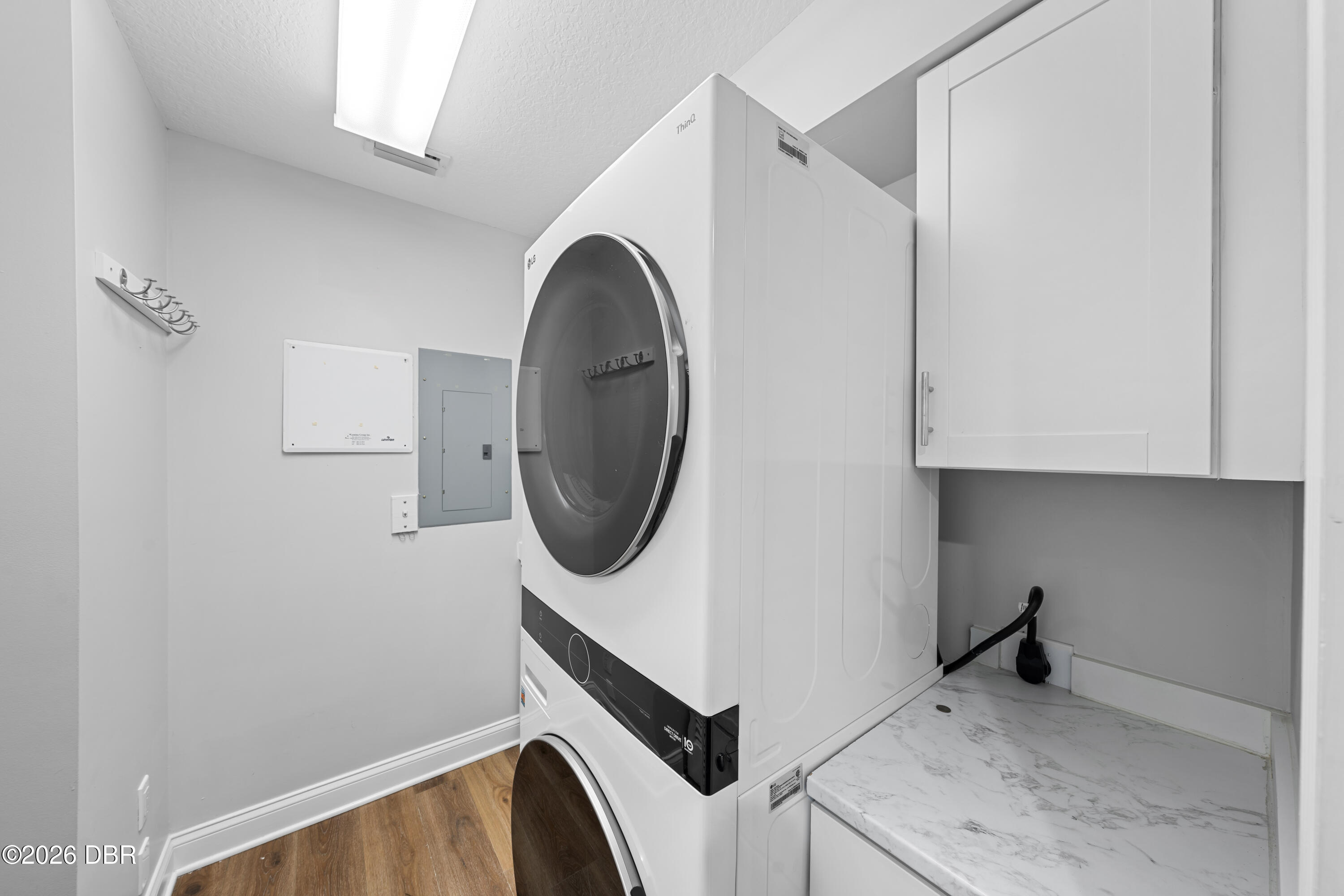 Laundry room with a stacked washer and dryer beside white cabinets and a marble-look counter.