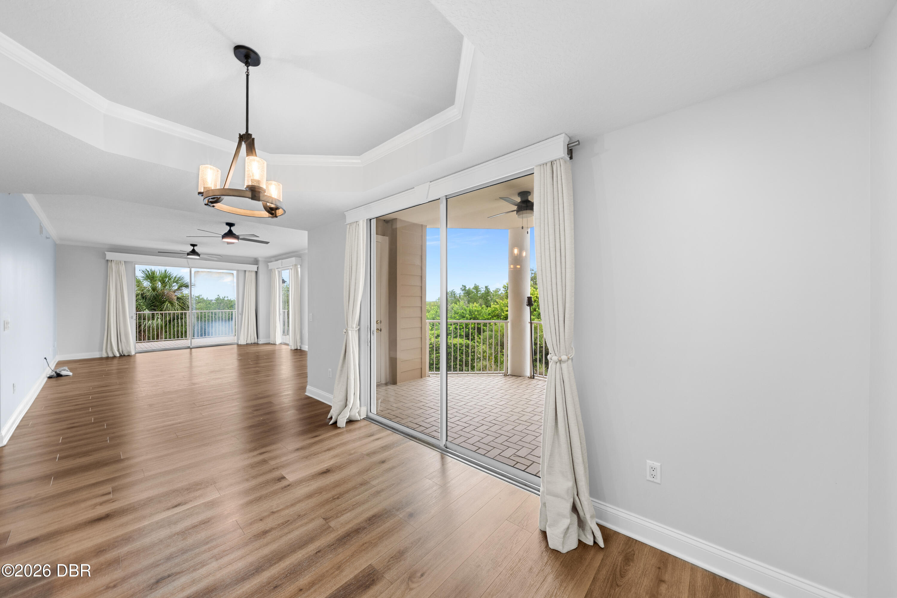 Empty living area with wood-look floors, tray ceiling, and sliding doors to a balcony with a water view.