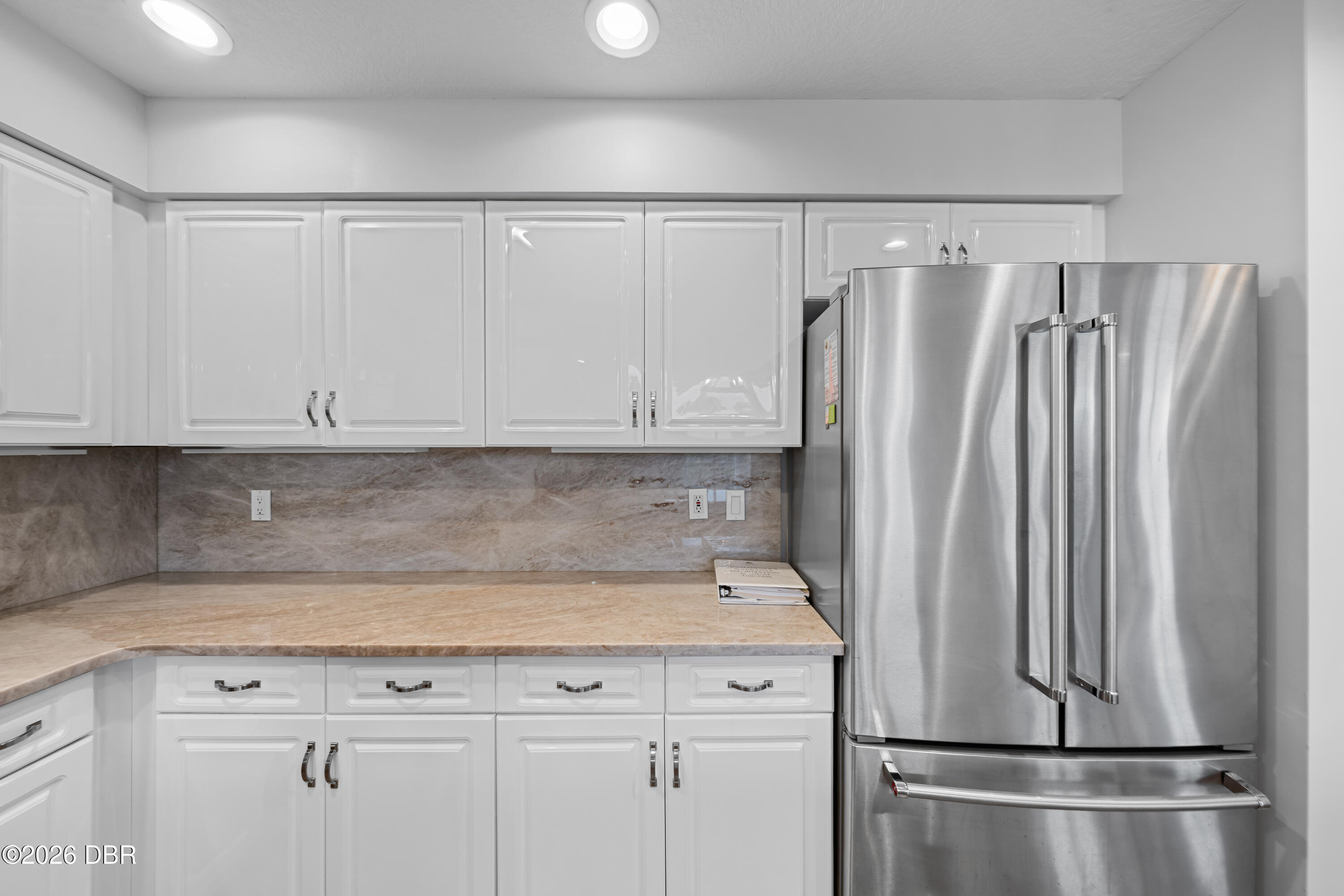 Kitchen with white cabinets, beige stone counters, and a stainless steel French-door refrigerator.