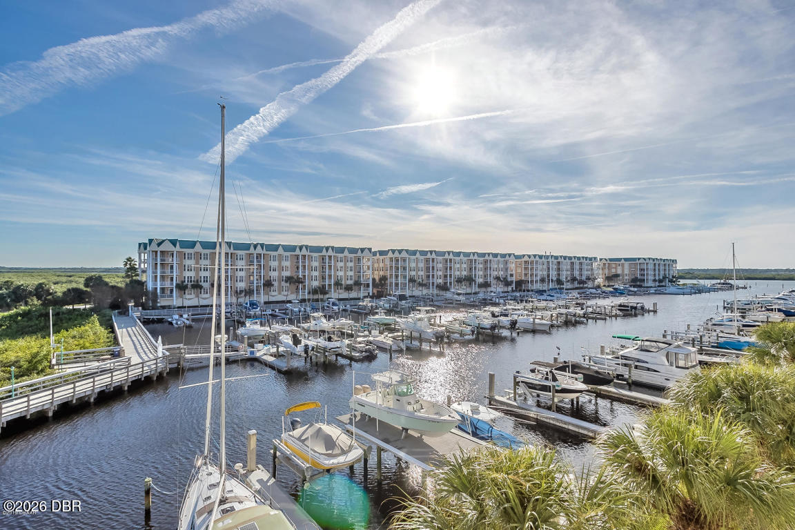 Condominium buildings line a marina filled with boats under a bright, cloud-streaked sky.