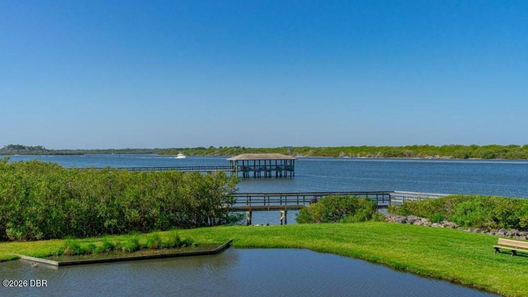 Waterfront view with grassy banks, wooden boardwalks, and a covered pavilion over the water.