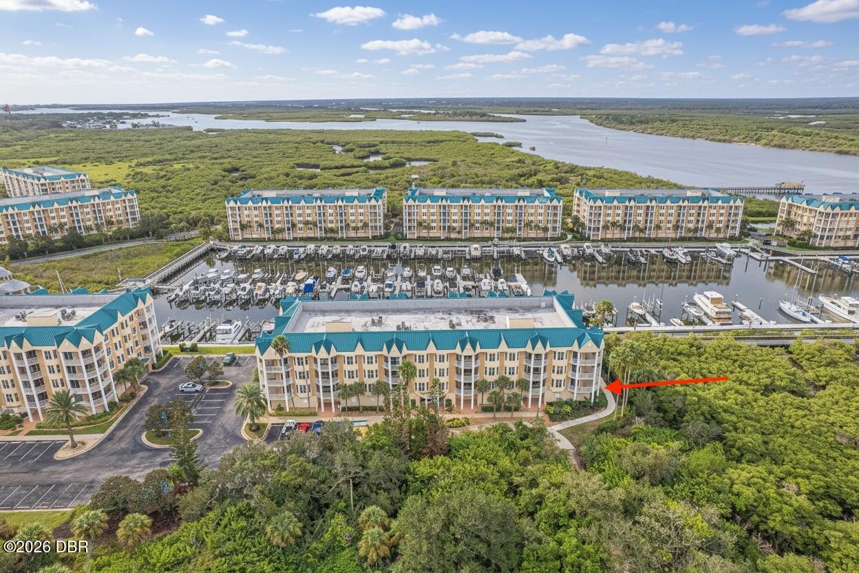 Aerial view of a condominium building beside a marina and wetlands, indicated by a red arrow.