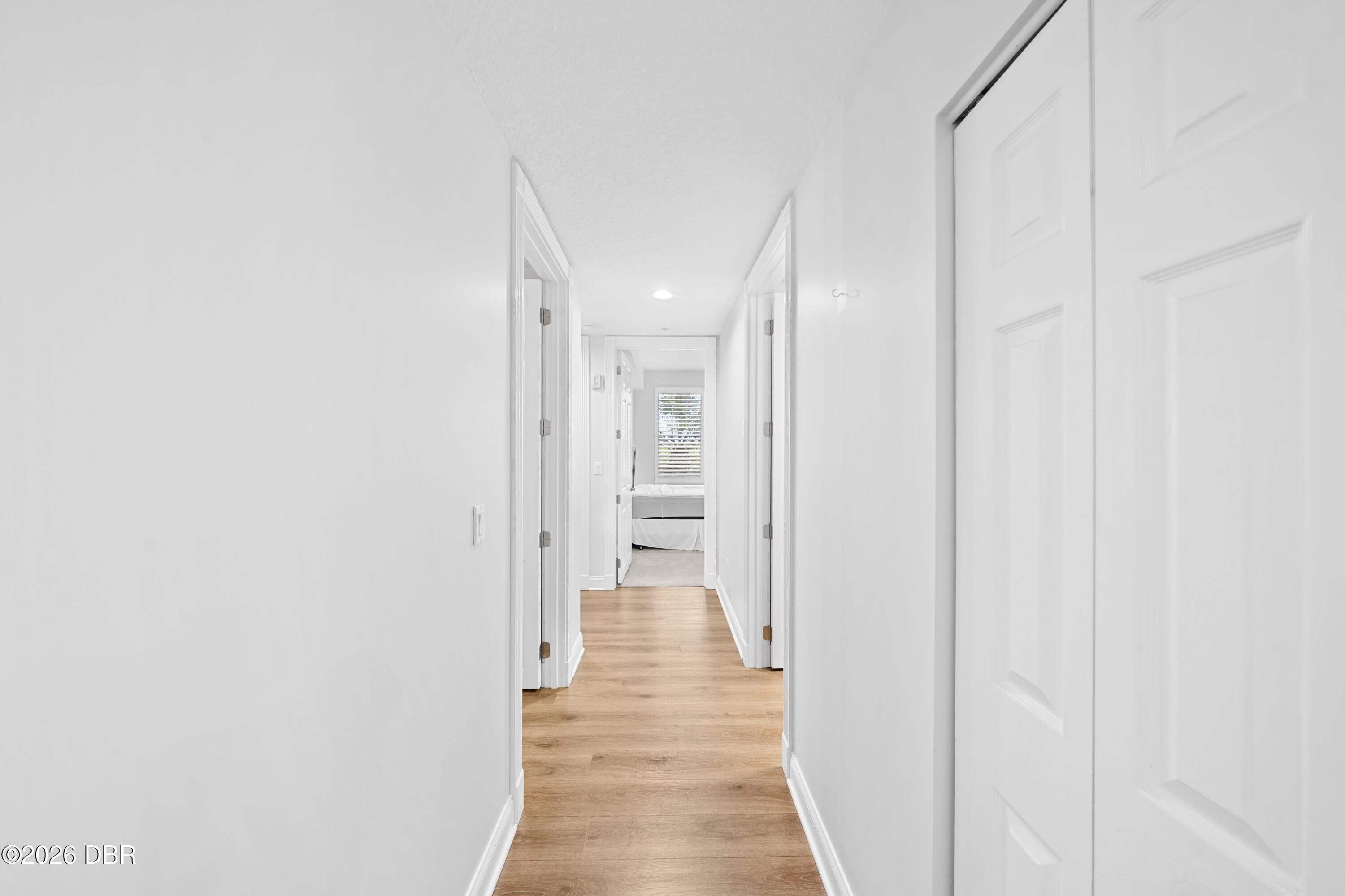 White hallway with light wood flooring and a bedroom visible at the far end.
