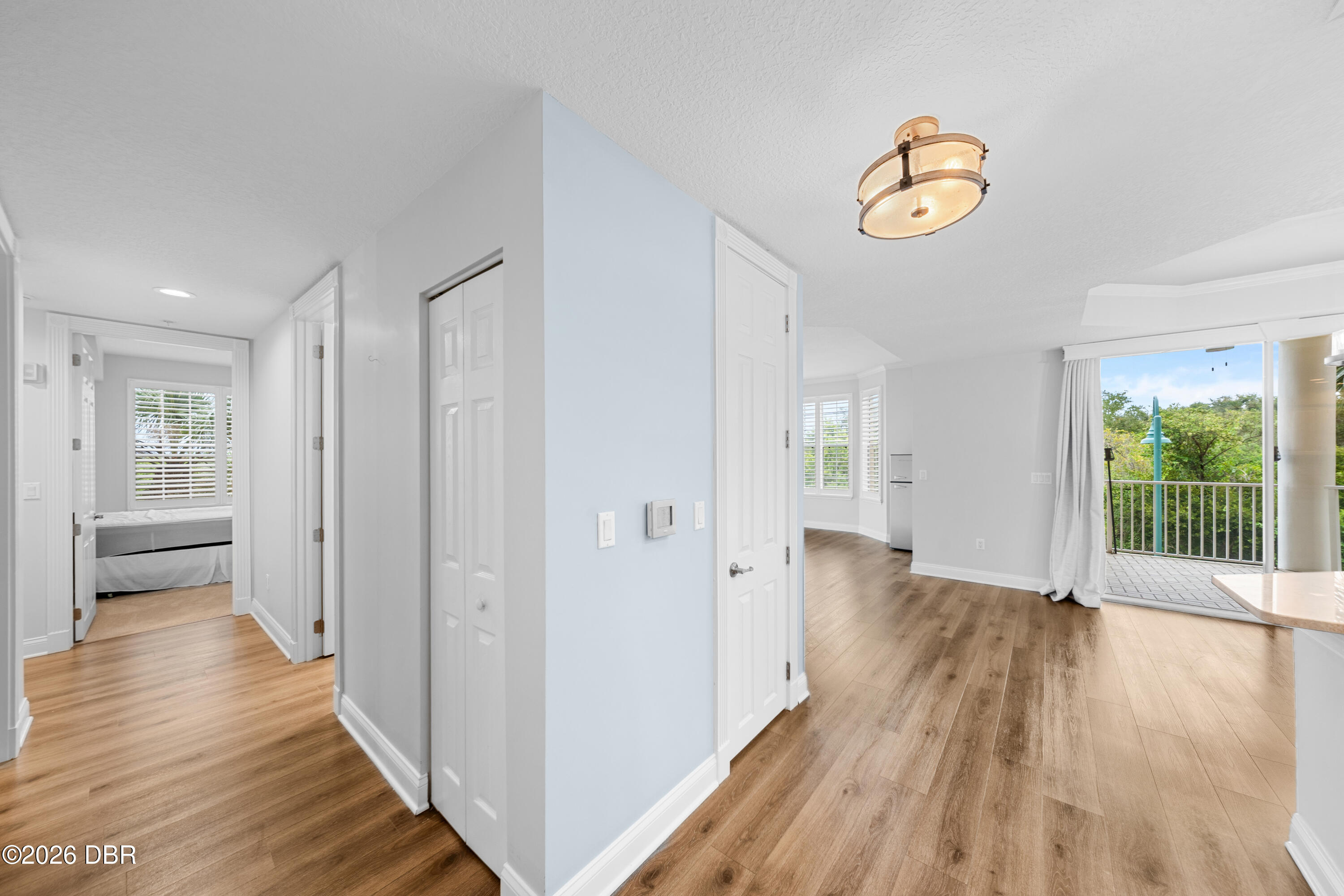 Condo hallway opens to a bright living area and balcony, with a bedroom visible through a doorway.