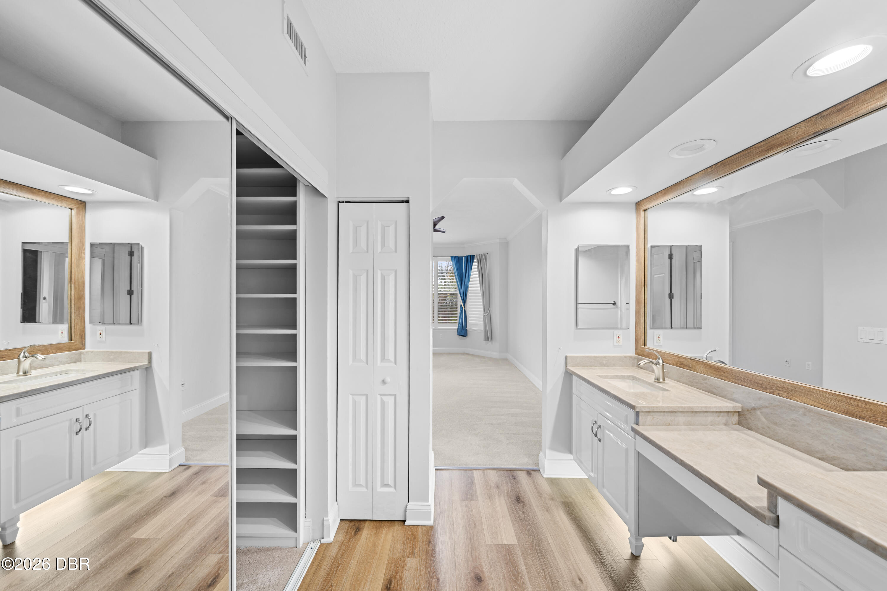 Bathroom dressing area with long stone vanities, wood-framed mirrors, and an open closet.