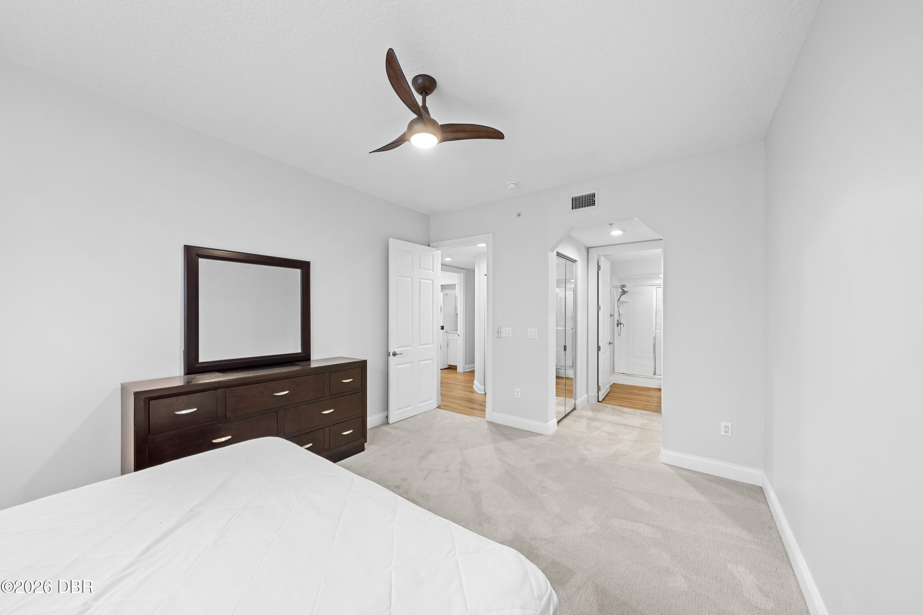 Bedroom with a dark wood dresser and mirror, ceiling fan, and open view into an adjoining bathroom.