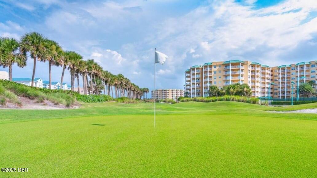 Golf course green with a flagstick, palm trees, and condominium buildings beyond.