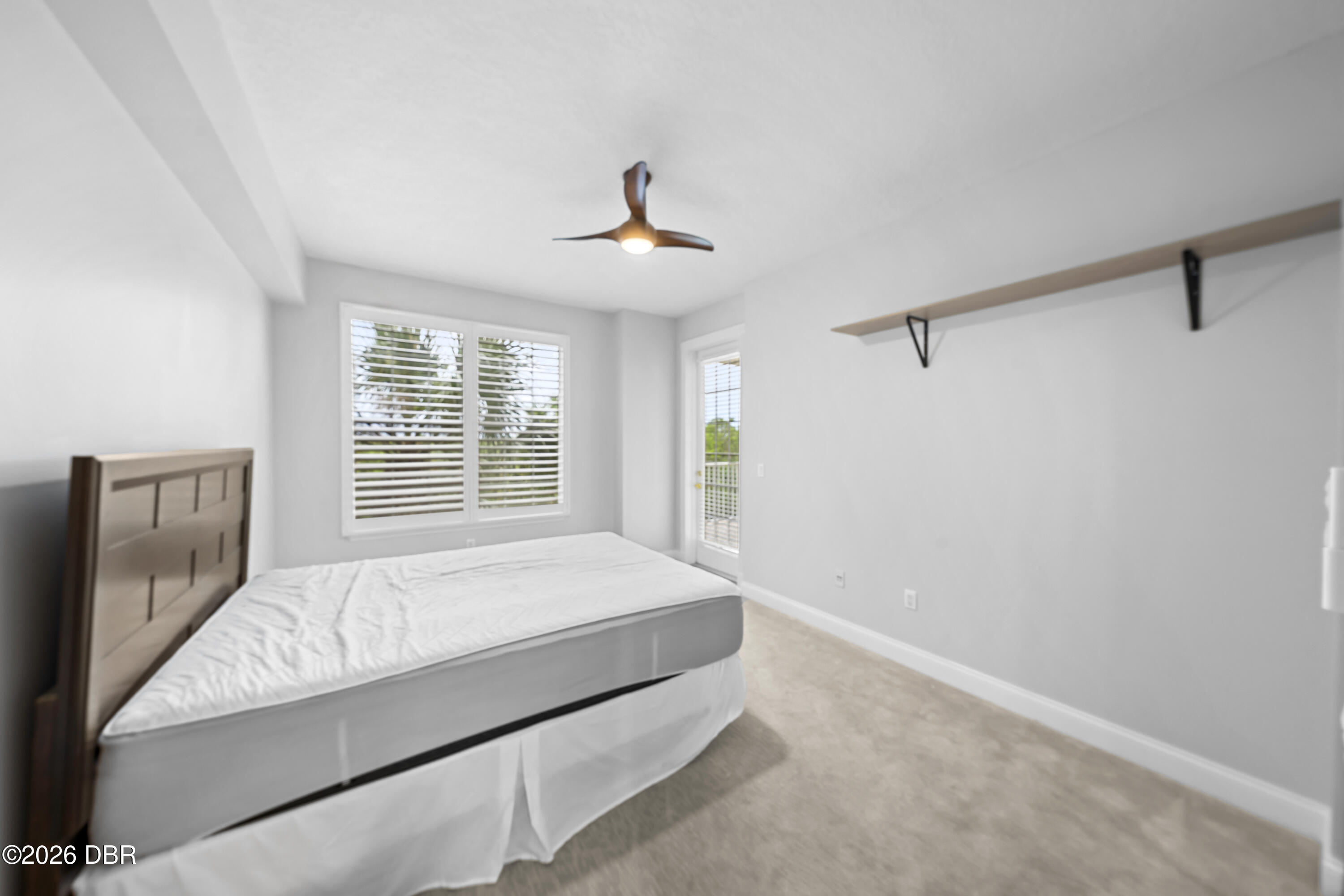 Bedroom with a bed beneath shuttered windows and a glass balcony door.