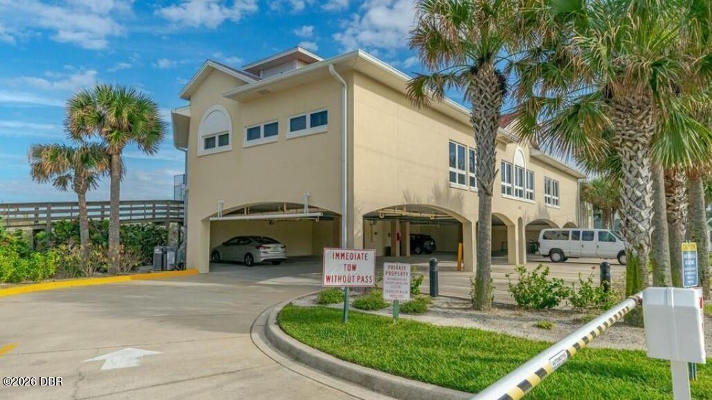 Tan two-story building with open parking bays, palm trees, and a curved driveway.