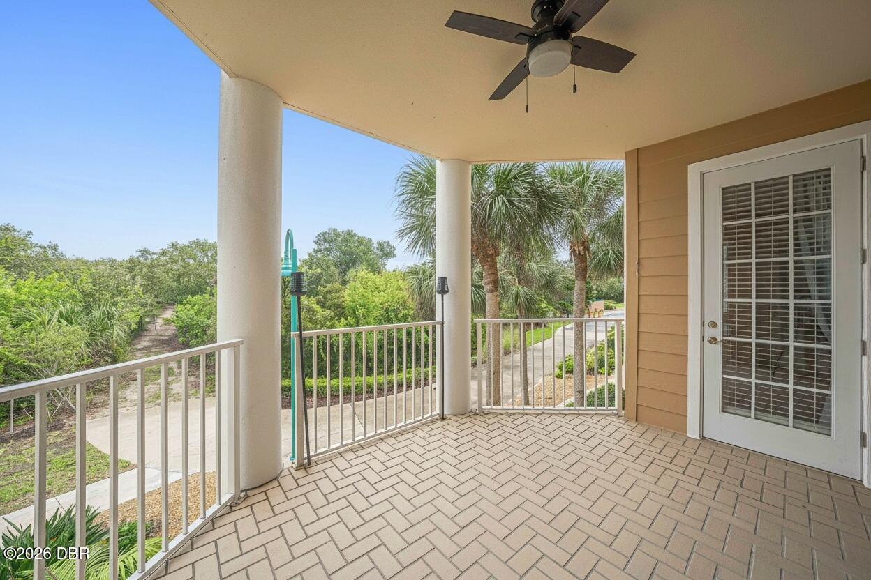 Covered tiled balcony with a ceiling fan, white railings, and palm trees beyond.