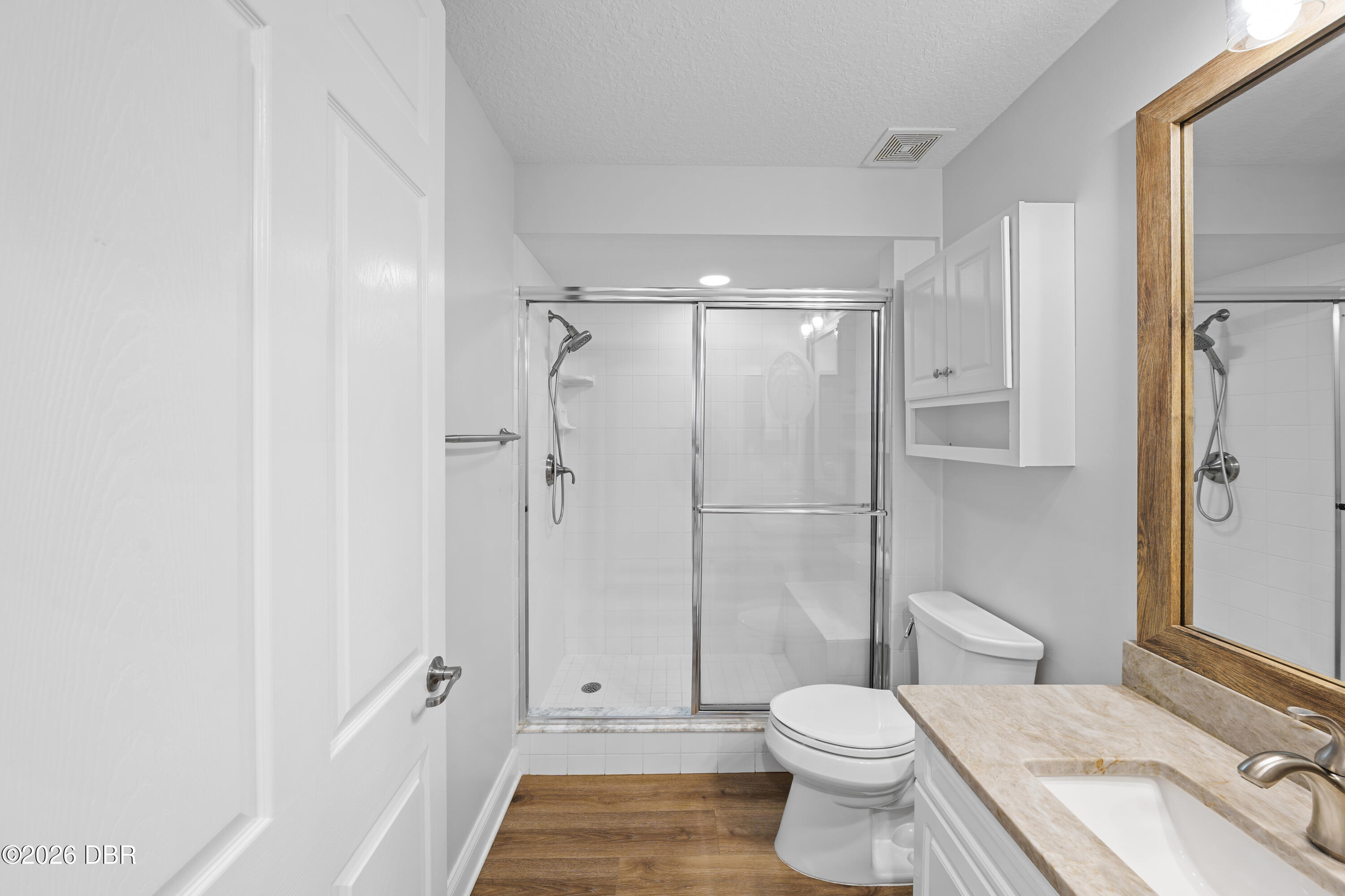 Bathroom with a glass-enclosed tiled shower, stone vanity counter, and warm wood-look flooring.