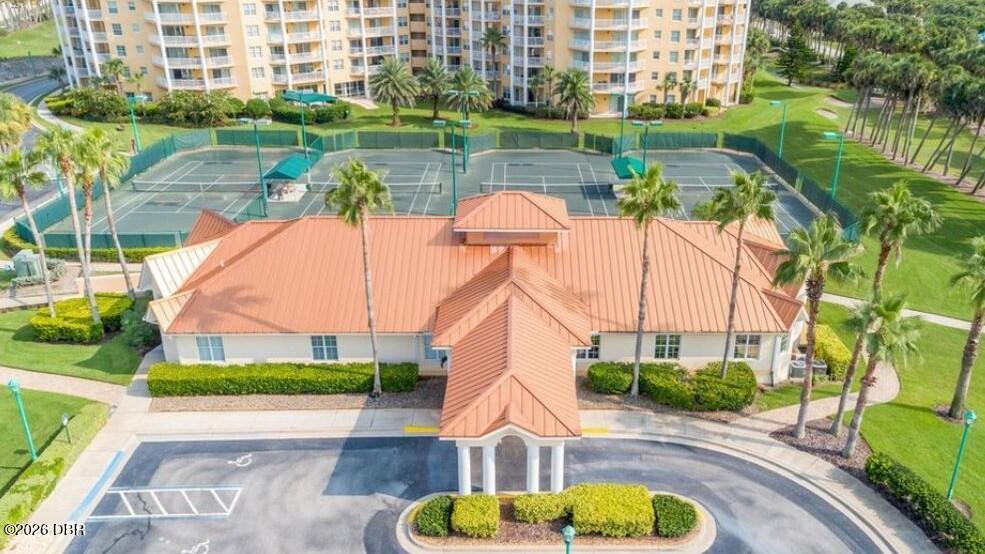 Condominium clubhouse and tennis courts beside a high-rise building, viewed from above.