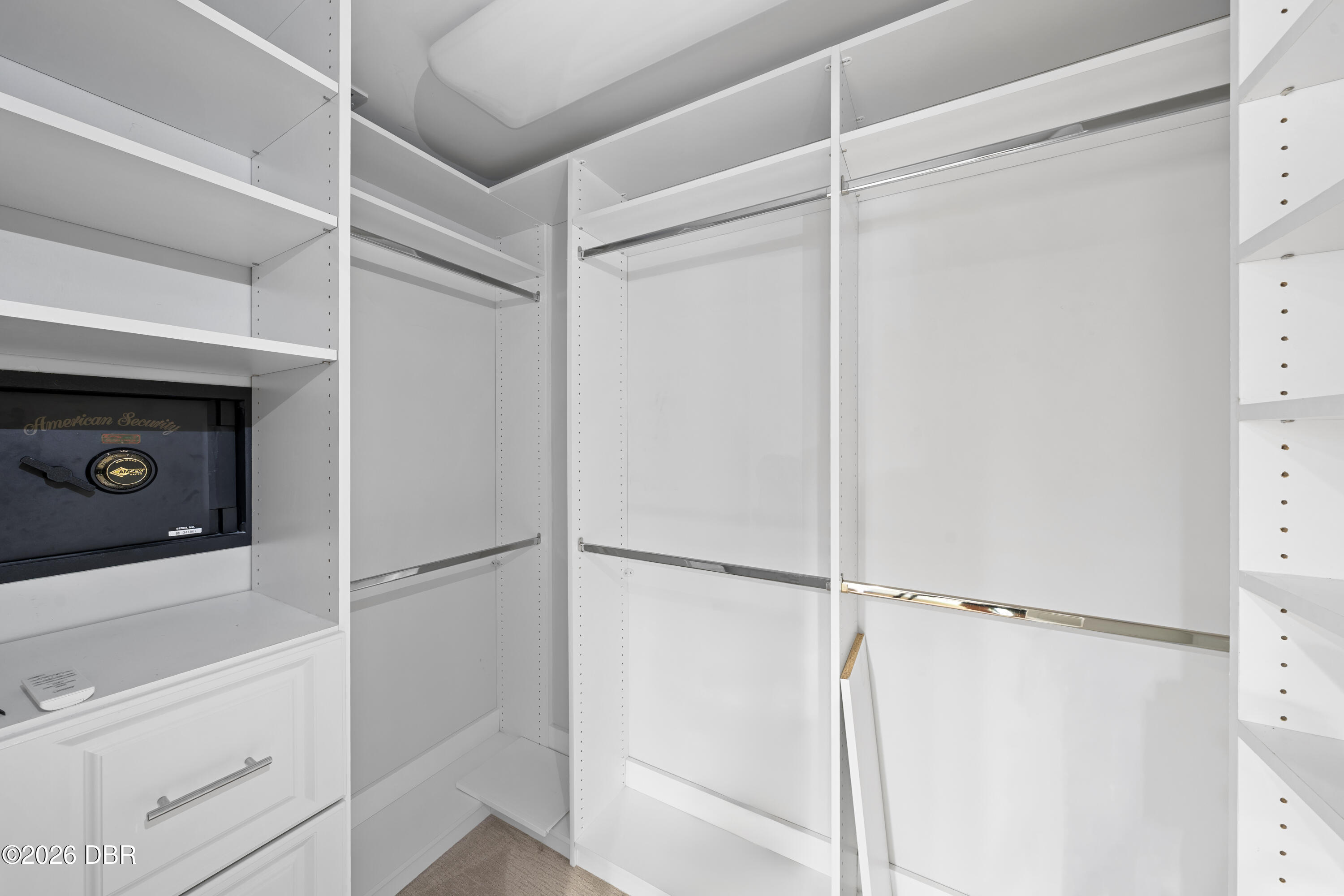Walk-in closet with white built-in shelving, chrome hanging rods, drawers, and a built-in safe.