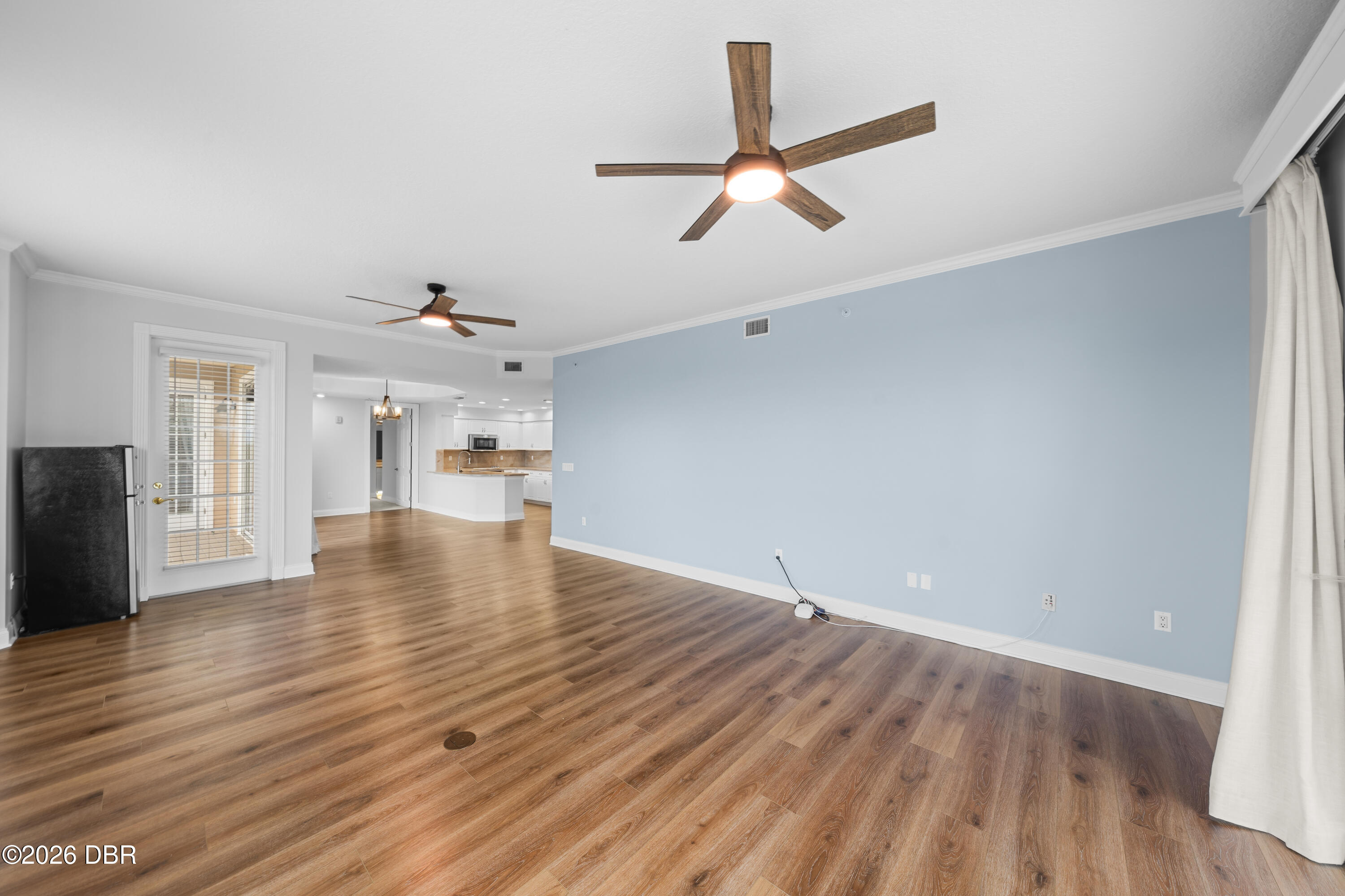 Empty living room with a blue accent wall, wood-look flooring, and two ceiling fans.