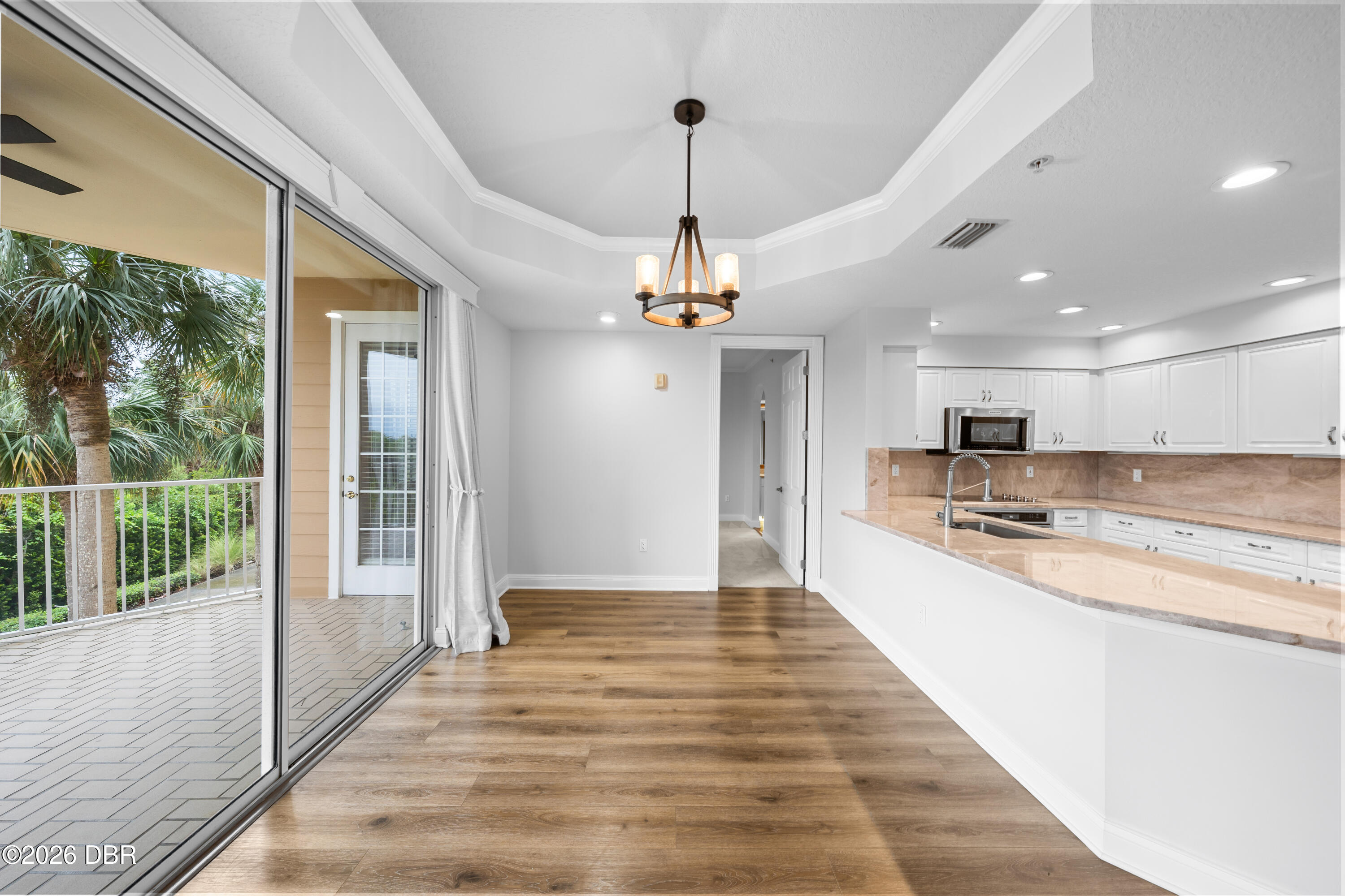 Vacant kitchen with white cabinets and stone breakfast bar beside a sliding door to a palm-lined balcony.