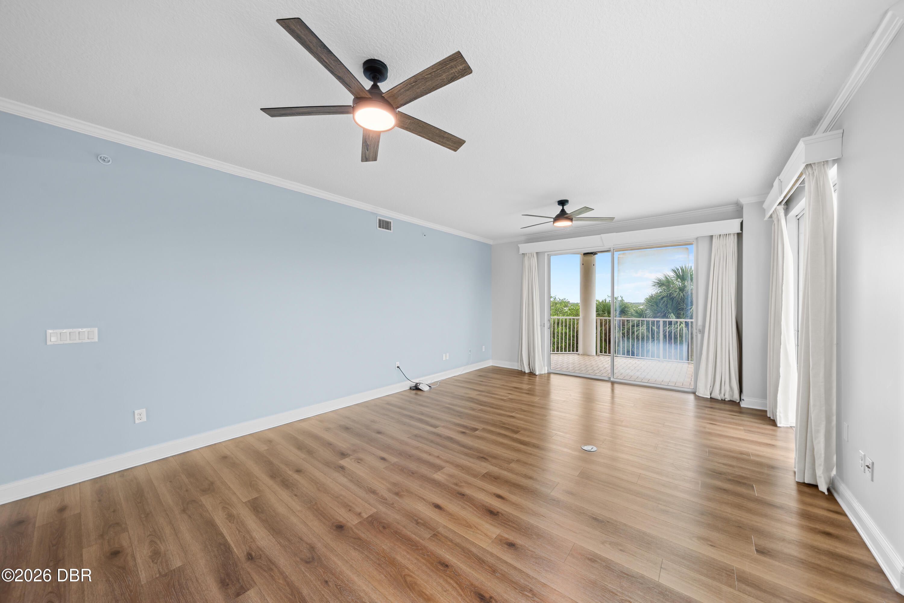 Vacant room with wood-look floors, two ceiling fans, and sliding doors to a balcony.